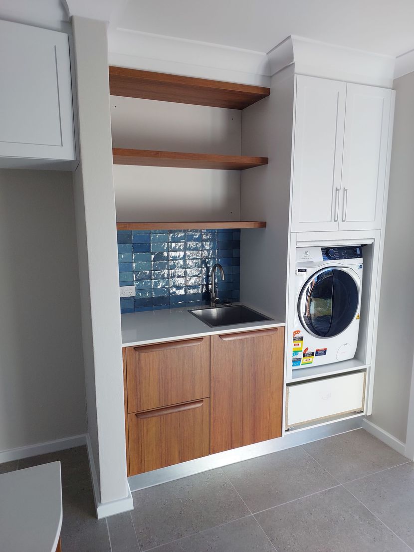 Laundry room with built-in cabinetry. White and wood cabinets, open shelves, blue tile backsplash, and washing machine.