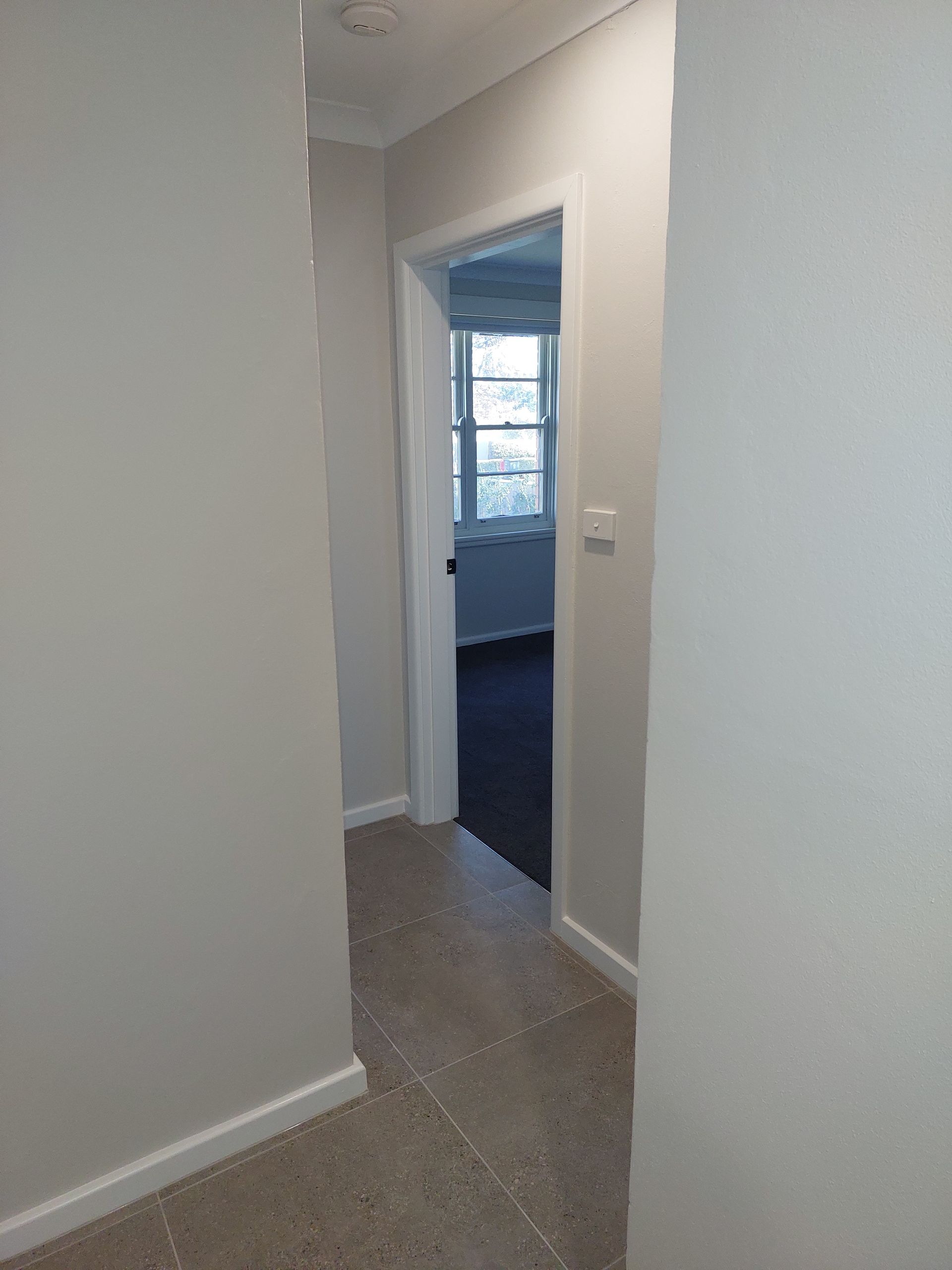 Narrow Hallway With Light Gray Walls and Beige Carpet Leading to a Room With a Window — Elimar Construction in Goulburn, NSW