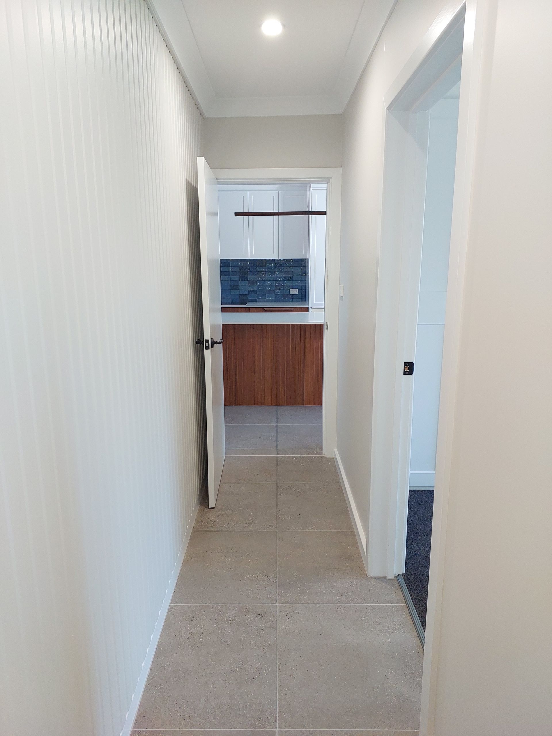 Narrow Hallway With Light-colored Walls and Flooring, Leading to a Kitchen With Wood Cabinets and Blue Tile Backsplash — Elimar Construction in Goulburn, NSW