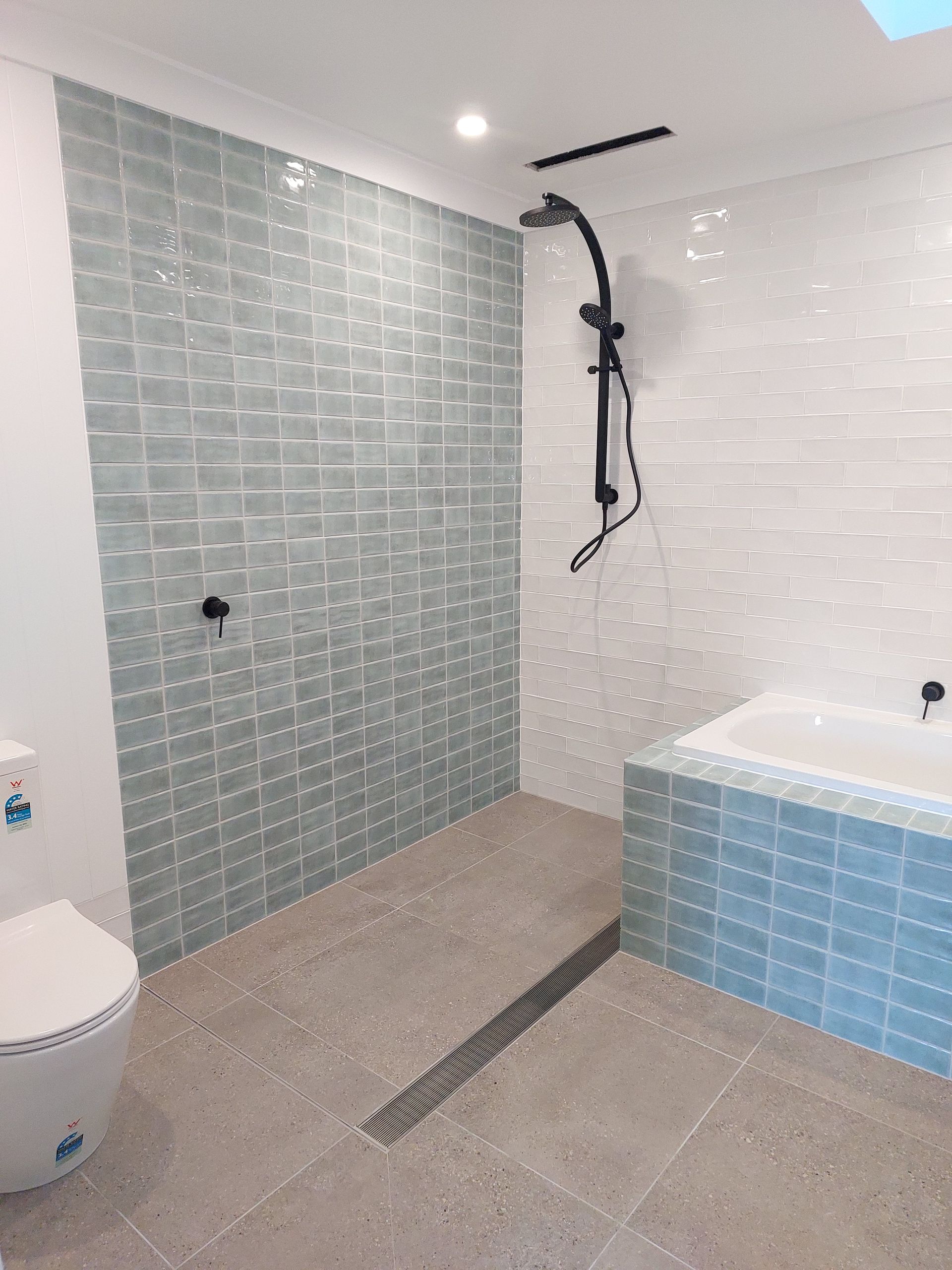 Bathroom With Light Blue Tile Shower, Dark Fixtures, and a Bathtub. Beige Floor — Elimar Construction in Goulburn, NSW
