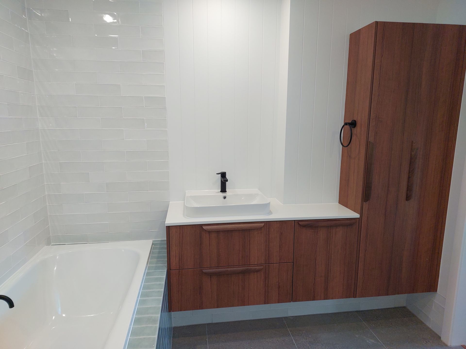 Bathroom With Wood Vanity and Tall Cabinet, White Tub, and Light-colored Tiled Walls — Elimar Construction in Goulburn, NSW