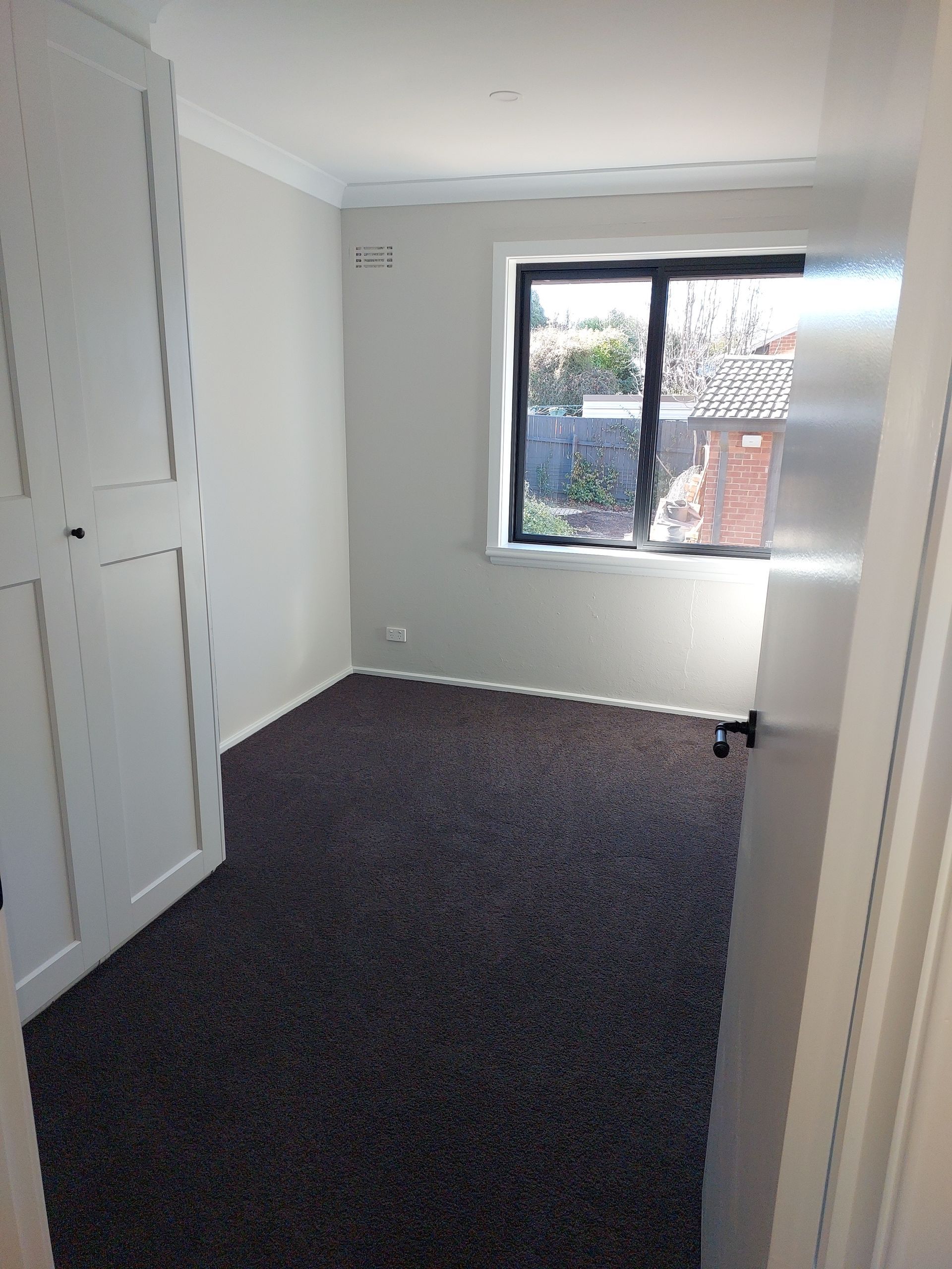 Empty Bedroom With Brown Carpet, Window, and White Closet — Elimar Construction in Goulburn, NSW