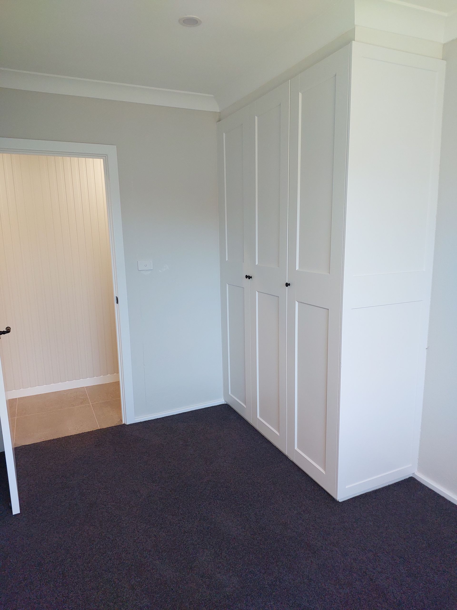White Built-in Closet With Six Doors in a Room With Gray Walls and a Dark Gray Carpet. Doorway to the Left — Elimar Construction in Goulburn, NSW