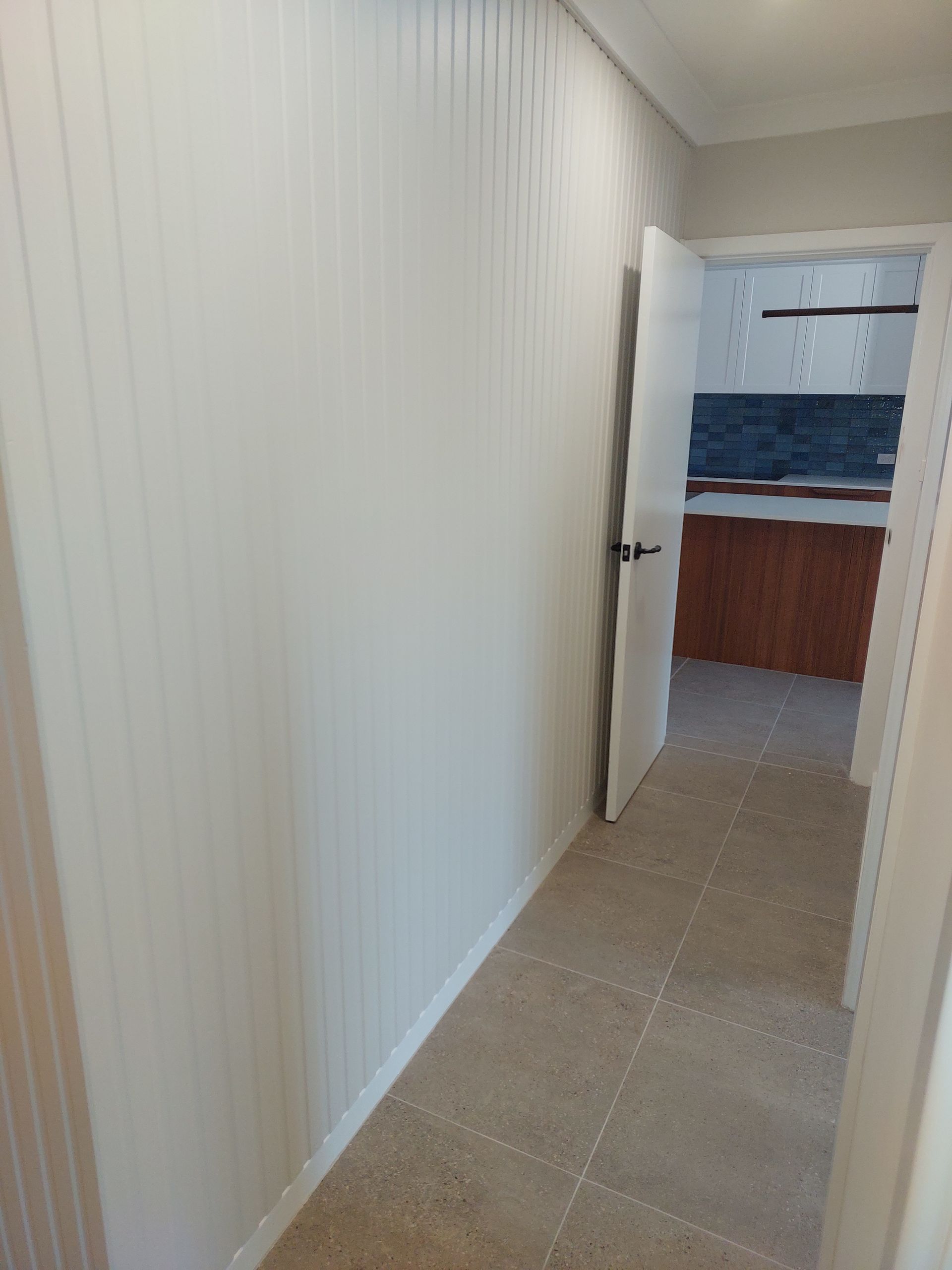 Hallway With White Paneled Walls, Leading to a Room With a Brown Cabinet and Blue Tile Backsplash — Elimar Construction in Goulburn, NSW