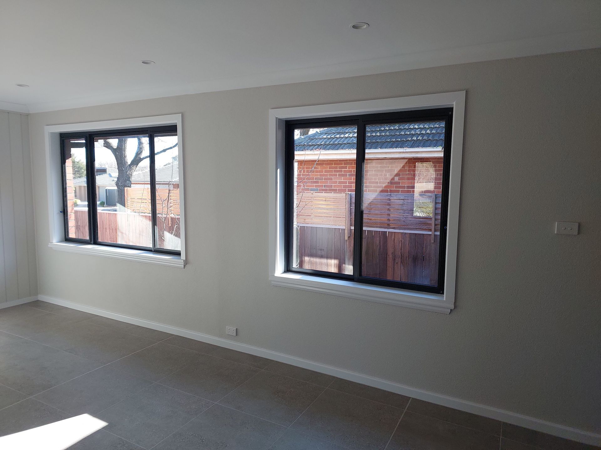 Two Windows With Dark Frames and White Trim in a Room With Light Gray Walls and Carpet — Elimar Construction in Goulburn, NSW