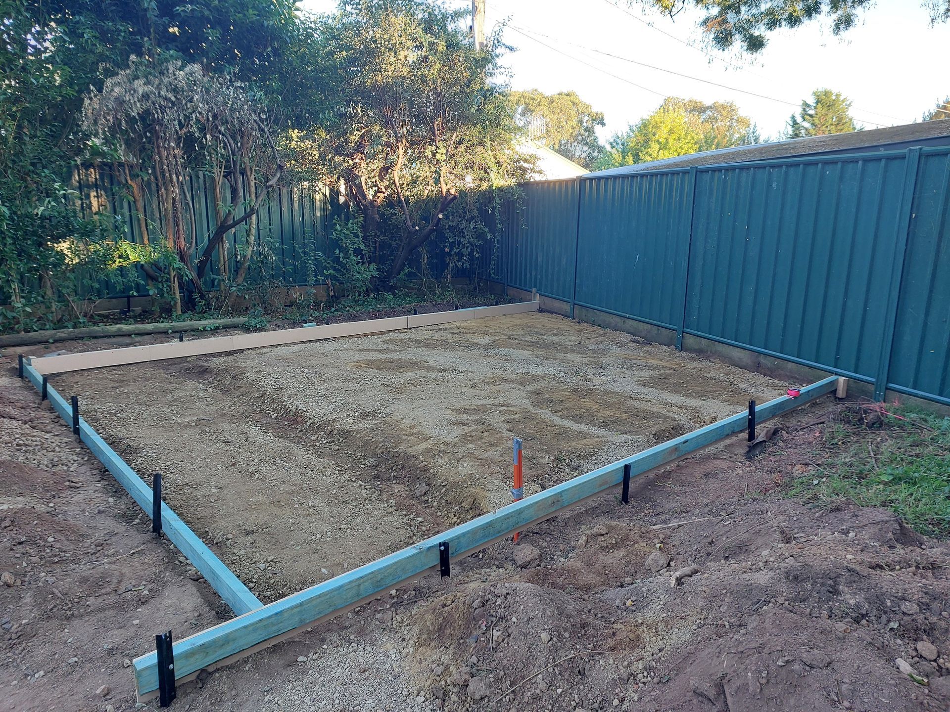 a Gravel-filled Rectangular Area Framed by Wooden Beams, Surrounded by Soil, Near a Green Fence — Elimar Construction in Goulburn, NSW
