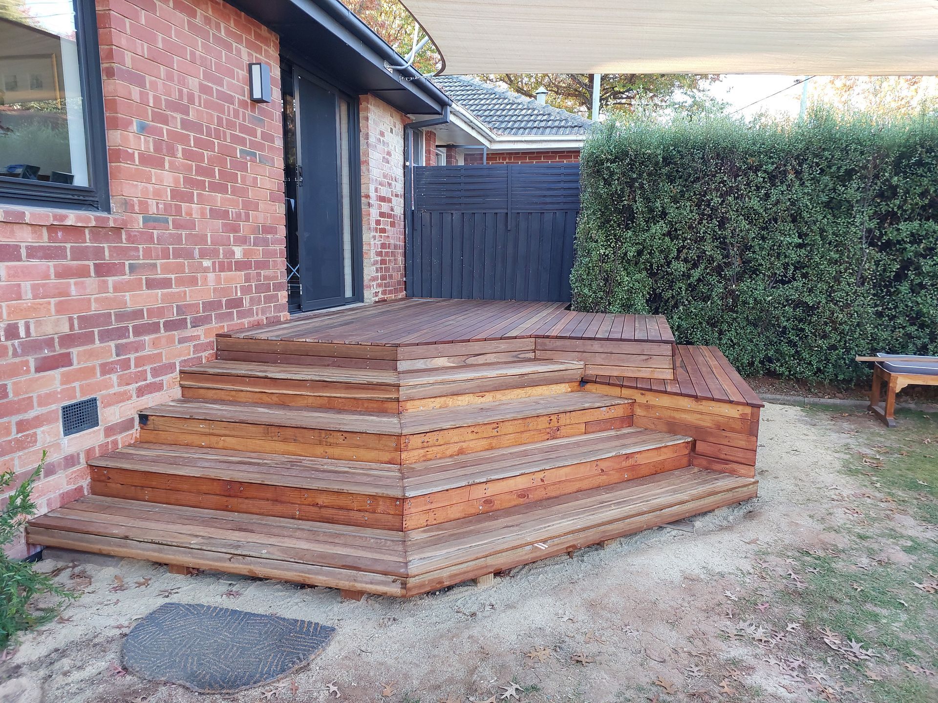 A Wooden Deck With Stairs is in Front of a Brick House — Elimar Construction in Goulburn, NSW