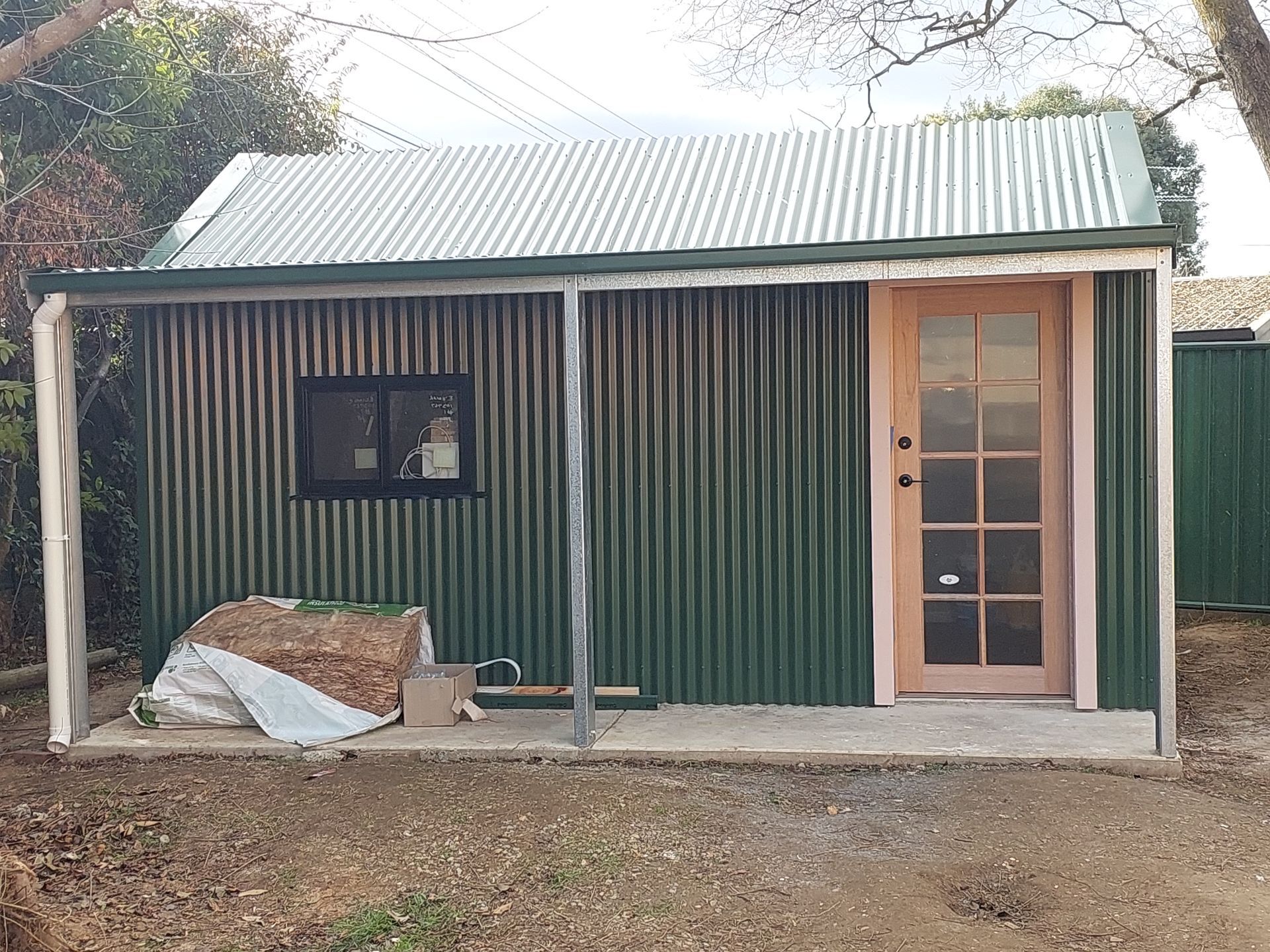 Green Corrugated Metal Shed With a Wooden Door, Window, and Small Porch — Elimar Construction in Goulburn, NSW