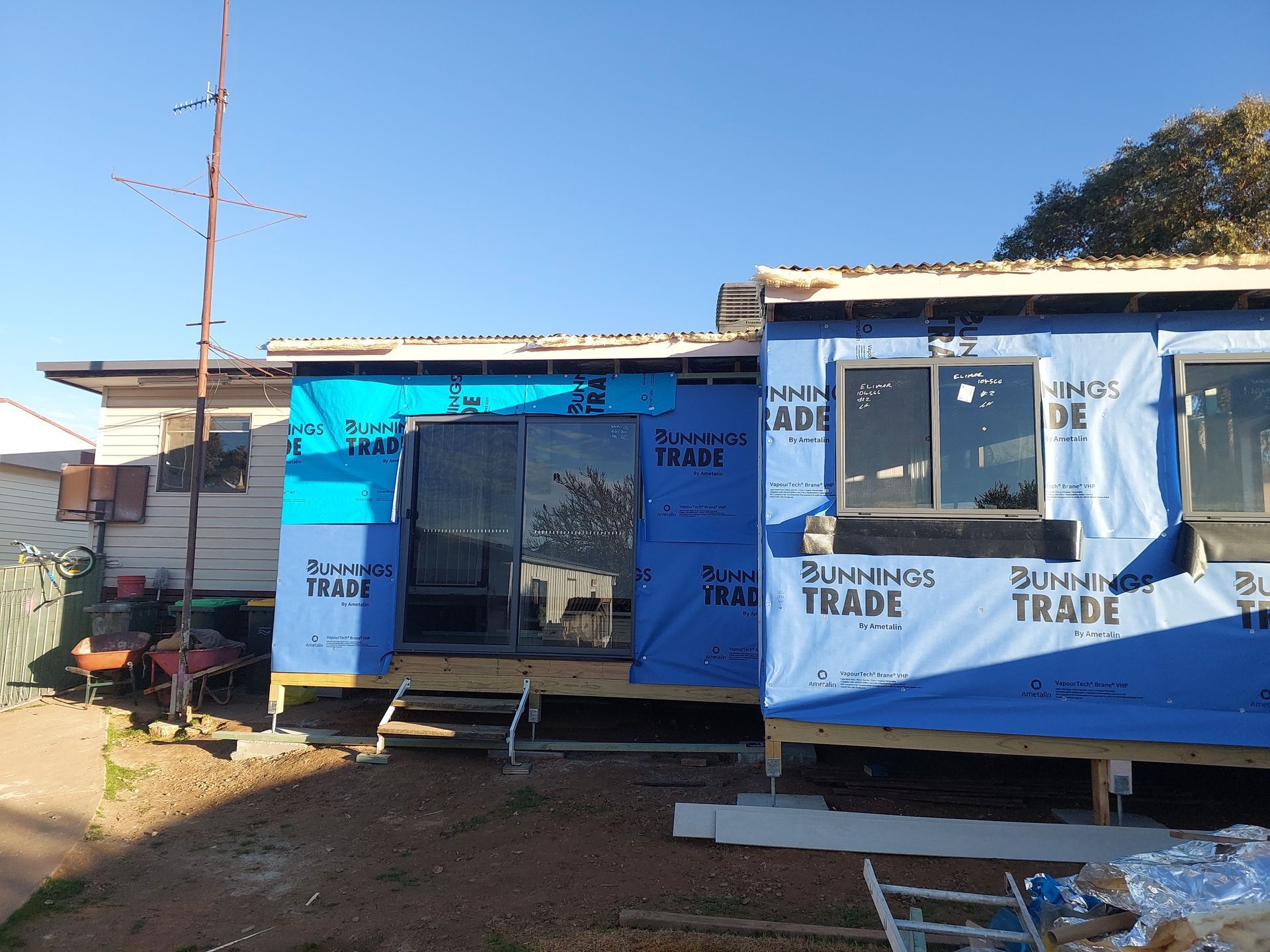 House Under Construction With Blue Protective Wrap, Wooden Frame, and Windows — Elimar Construction in Goulburn, NSW
