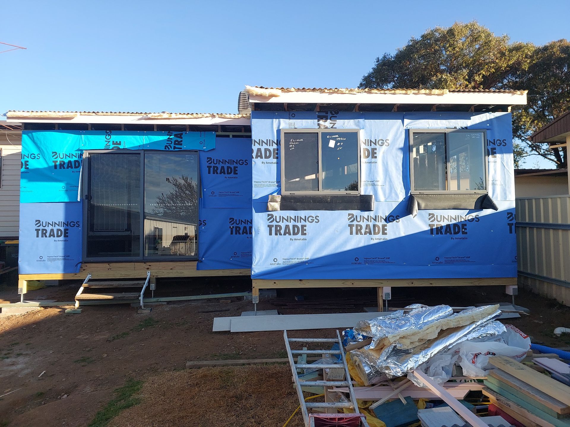 Construction Site: Framed House With Blue Wrap, Windows, and Debris on the Ground — Elimar Construction in Goulburn, NSW
