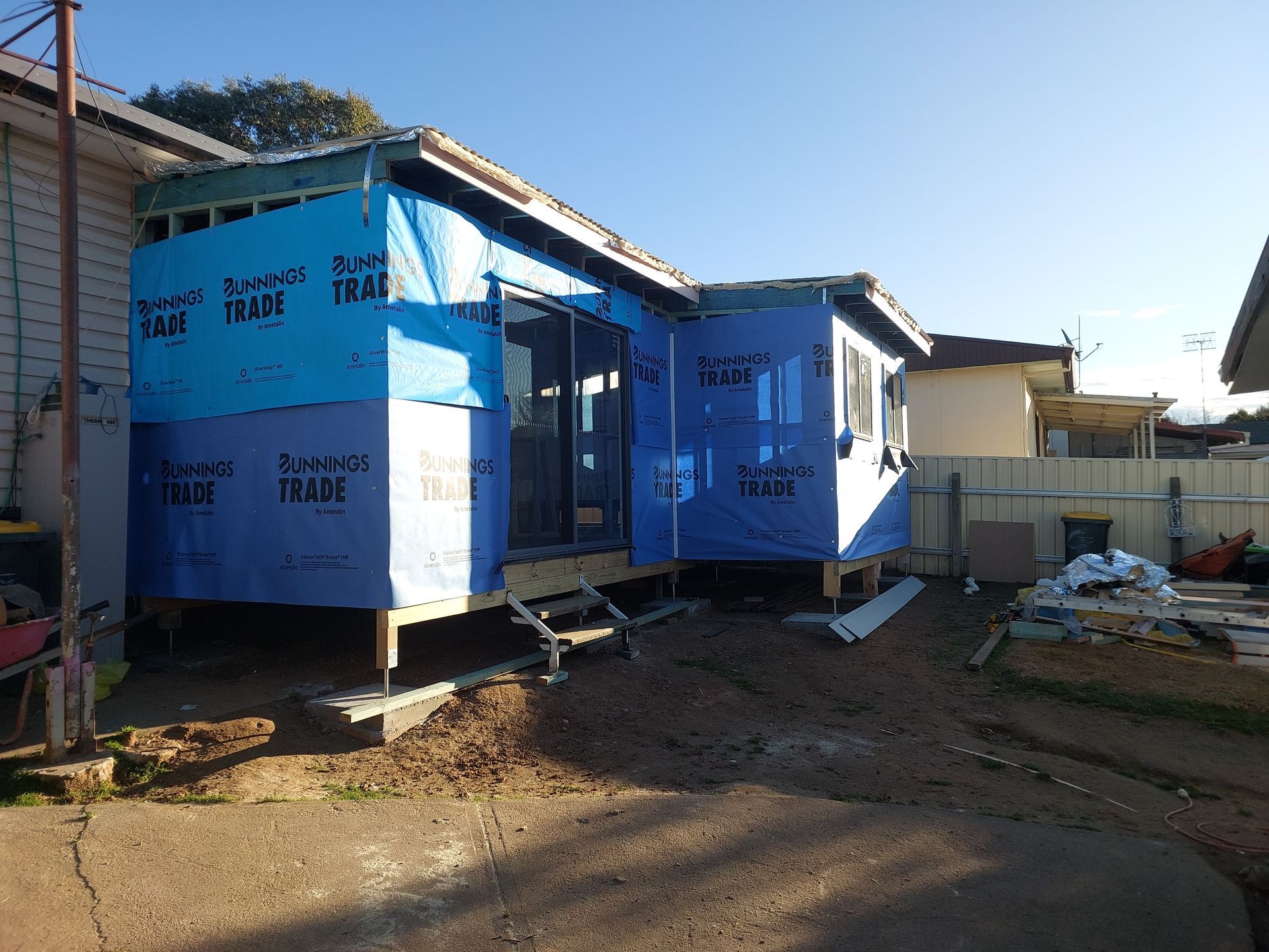 Construction of a House Extension, Framed With Blue Wrap, on a Brown, Dirt Lot — Elimar Construction in Goulburn, NSW