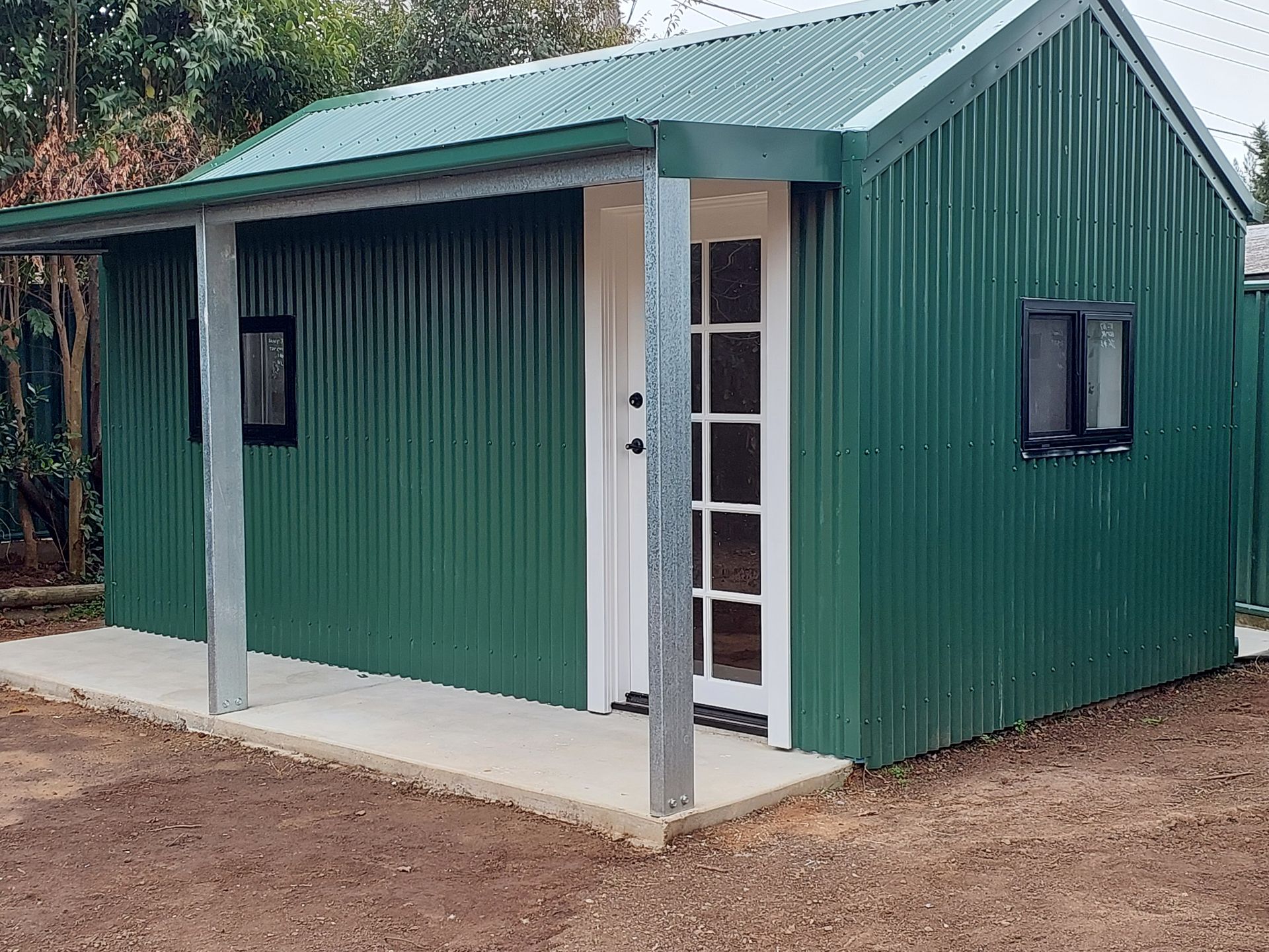 Green Corrugated Metal Shed With White Door, Two Windows, and Porch Roof — Elimar Construction in Goulburn, NSW