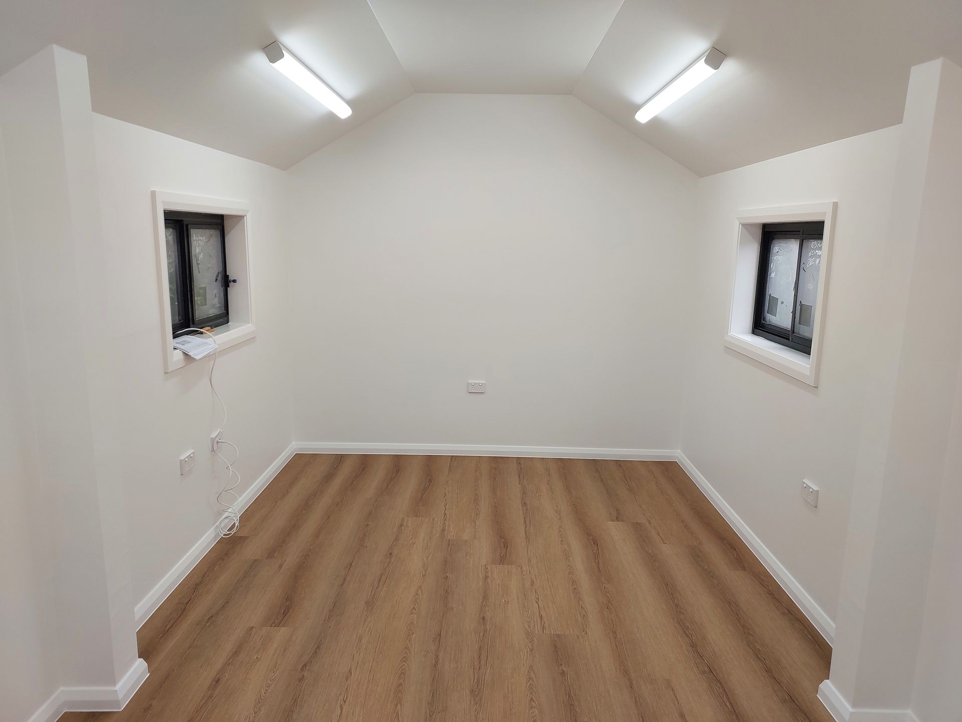 Empty Room With Light Wood Floor, Two Small Windows, and Overhead Lights — Elimar Construction in Goulburn, NSW