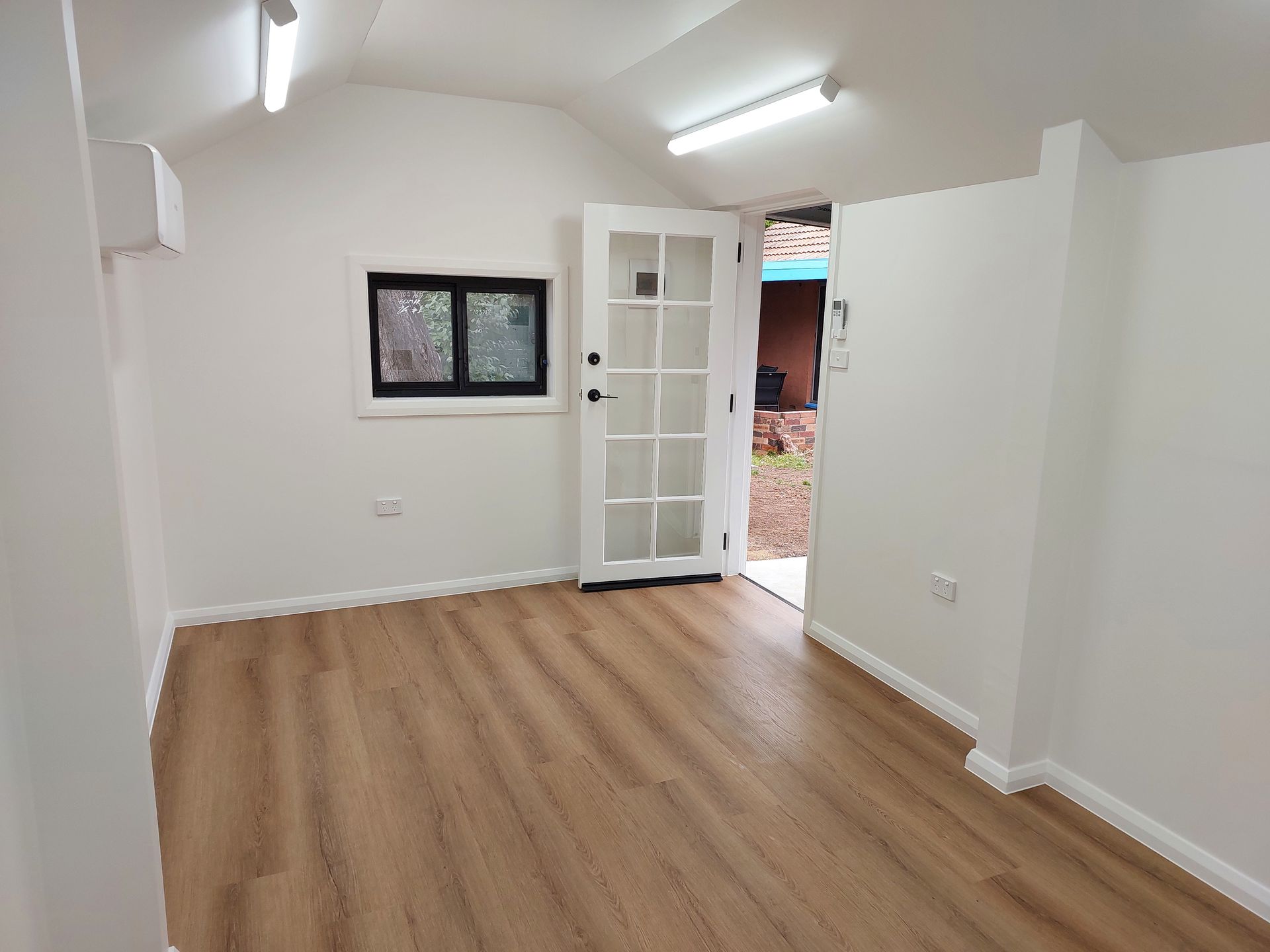 Interior of a Small, White Room With Wood-look Flooring, a Window, and a Glass-paneled Door Open to Outside — Elimar Construction in Goulburn, NSW
