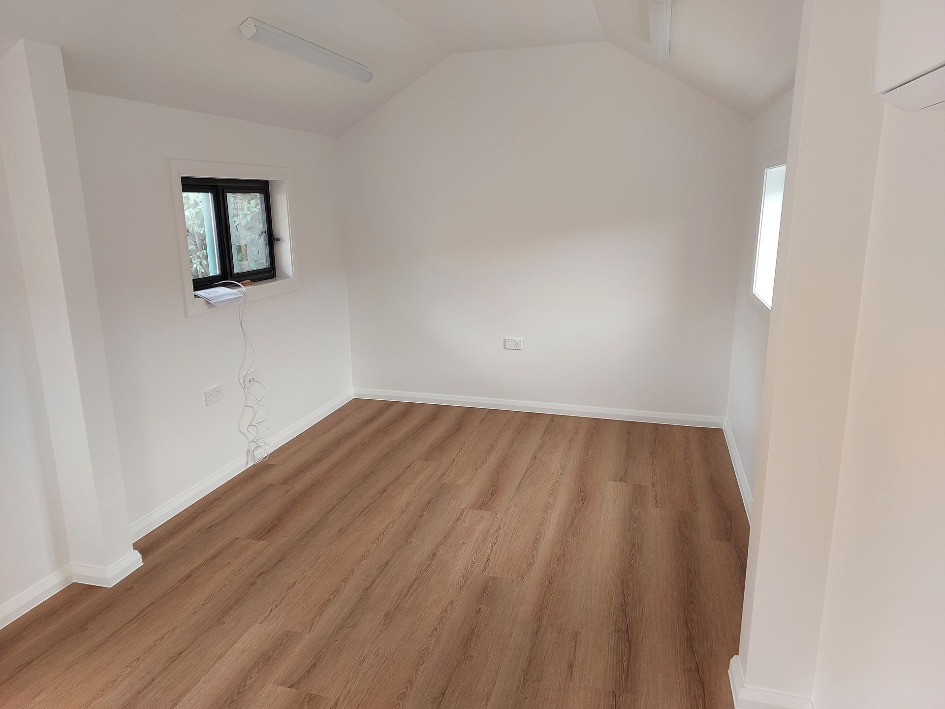 Empty Room With Light Wood Floor, White Walls, Small Window, and Angled Ceiling — Elimar Construction in Goulburn, NSW