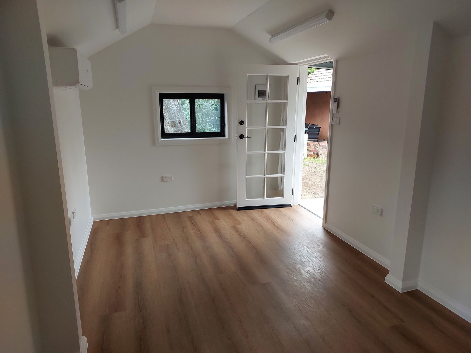 Empty, Bright Room With Wood-look Flooring, White Walls, and a Glass-paned Door Open to the Outdoors — Elimar Construction in Goulburn, NSW