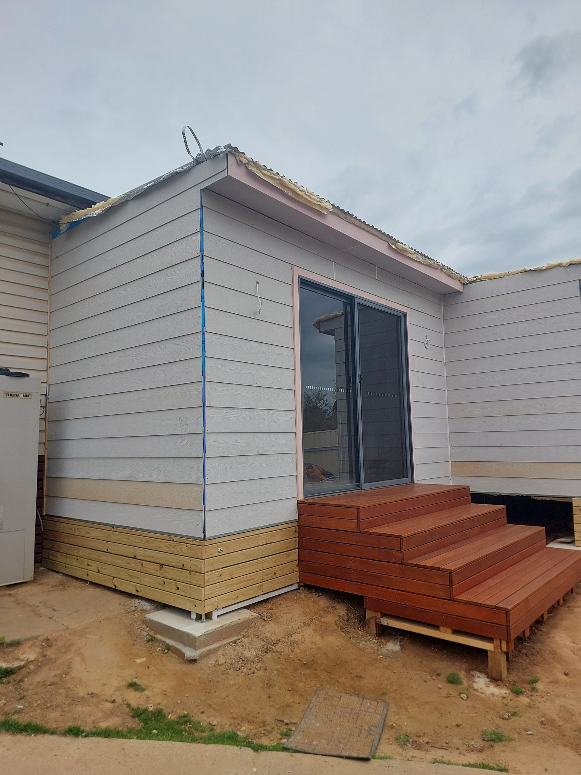 Exterior of a House Under Construction; White Siding, Wooden Deck Steps, and Sliding Glass Door — Elimar Construction in Goulburn, NSW