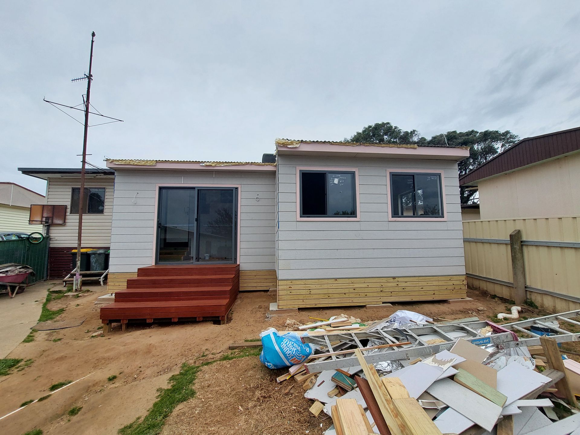 a House Undergoing Renovation, With Exposed Framing and Debris. Red Deck, Grey Siding, and Dark Windows — Elimar Construction in Goulburn, NSW