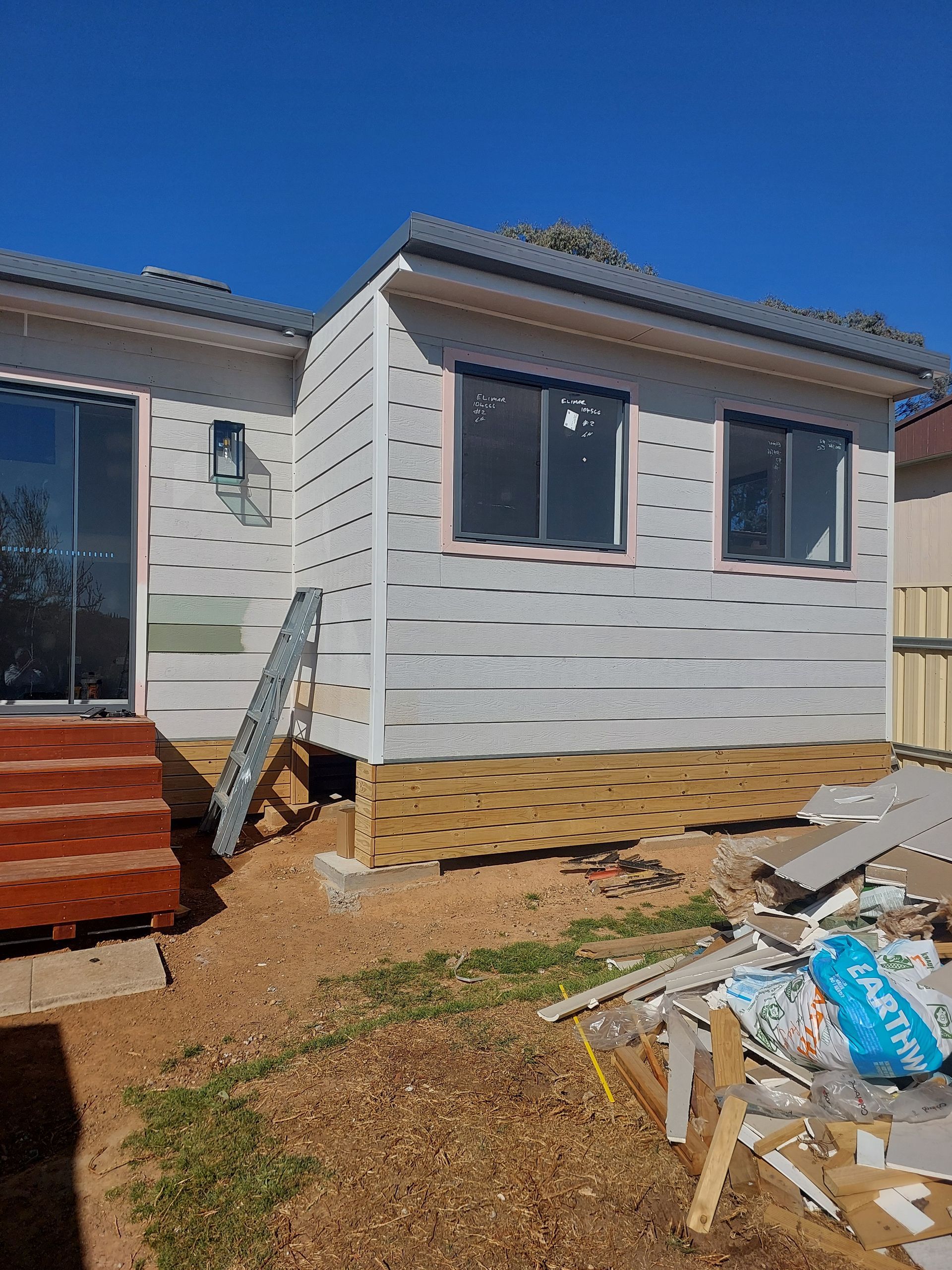 Exterior of a House Under Construction. Light Gray Siding, Windows, Small Deck, Ladder, Blue Sky — Elimar Construction in Goulburn, NSW