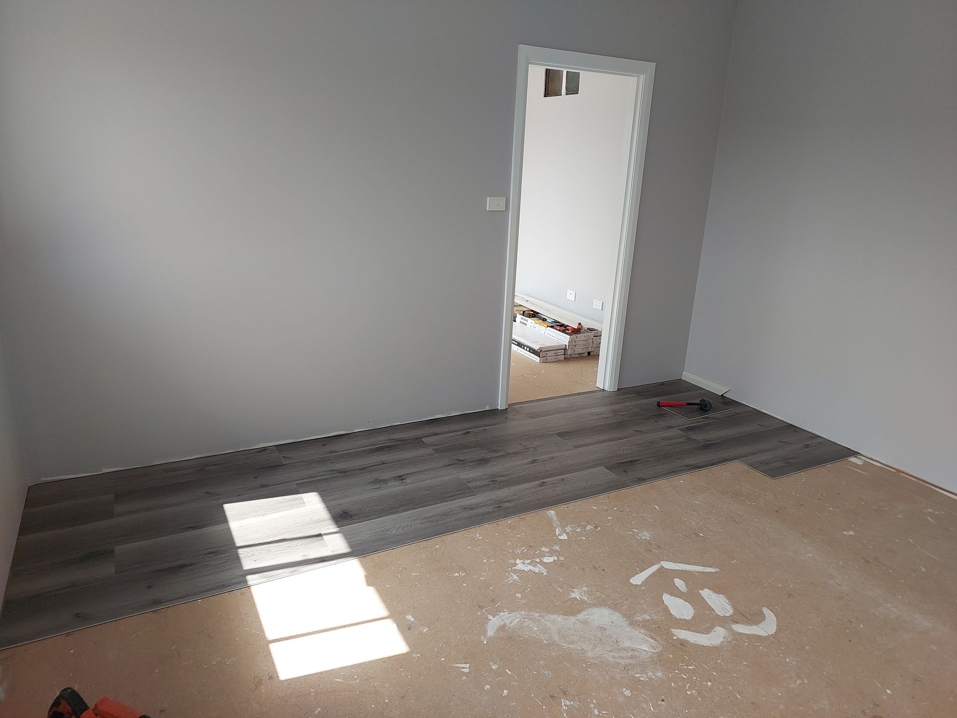 Room With Gray Walls and Wood-look Flooring Being Installed; Open Doorway Leads to Another Room — Elimar Construction in Goulburn, NSW