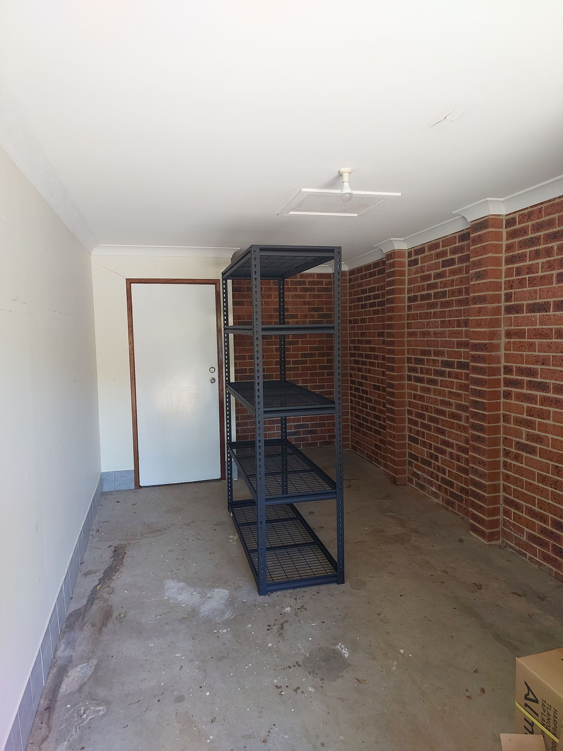 Empty Garage With a Metal Storage Shelf. the Walls Are White and Brick-patterned — Elimar Construction in Goulburn, NSW