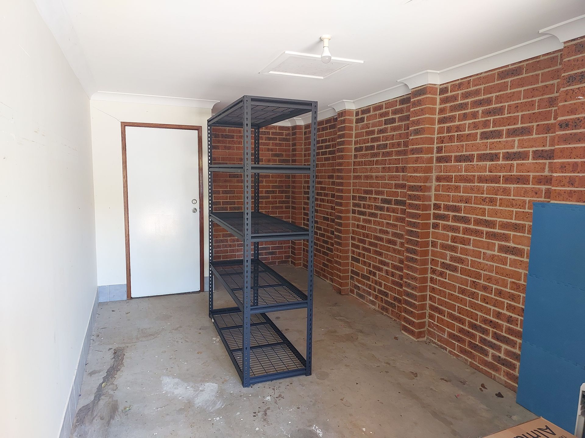 Garage Interior With Brick Wall, Metal Shelving Unit, and a White Door — Elimar Construction in Goulburn, NSW