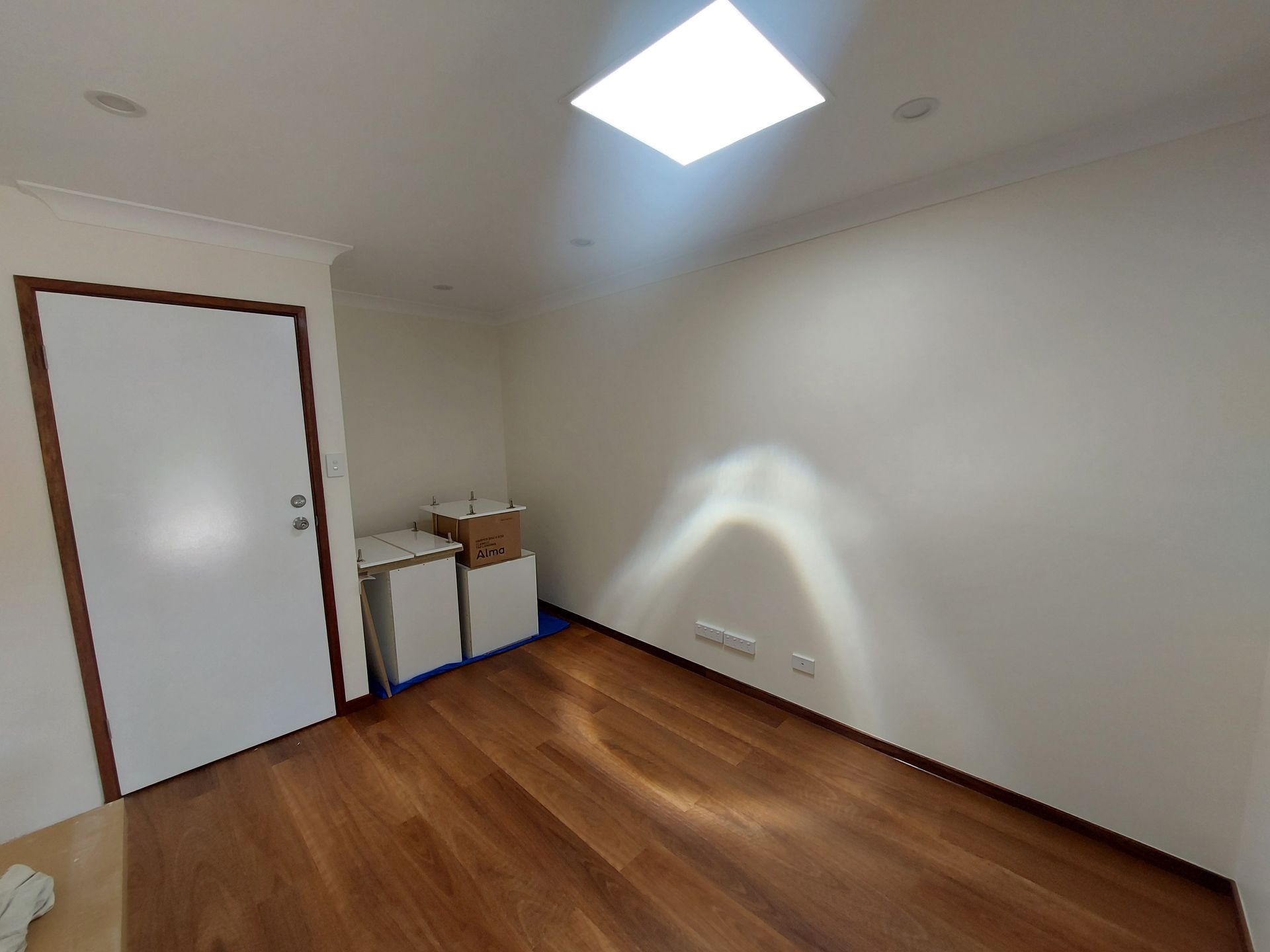 Empty Room With Wood Floor and a Bright Skylight. White Walls, a Closed Door, and Some Boxes Are Visible — Elimar Construction in Goulburn, NSW