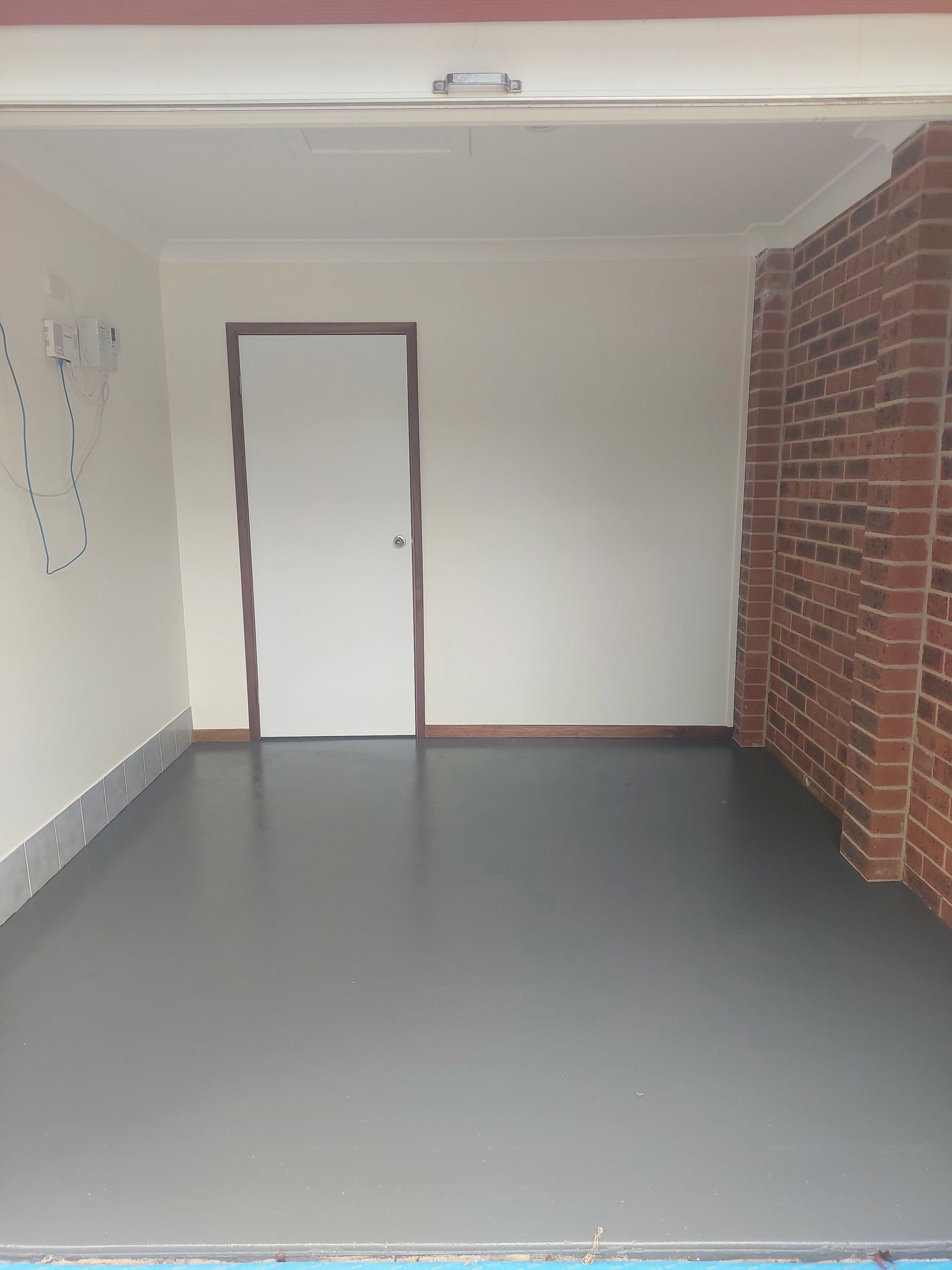 Empty Garage Interior With Gray Floor, White Walls, a Brick Column, and a Closed White Door — Elimar Construction in Goulburn, NSW