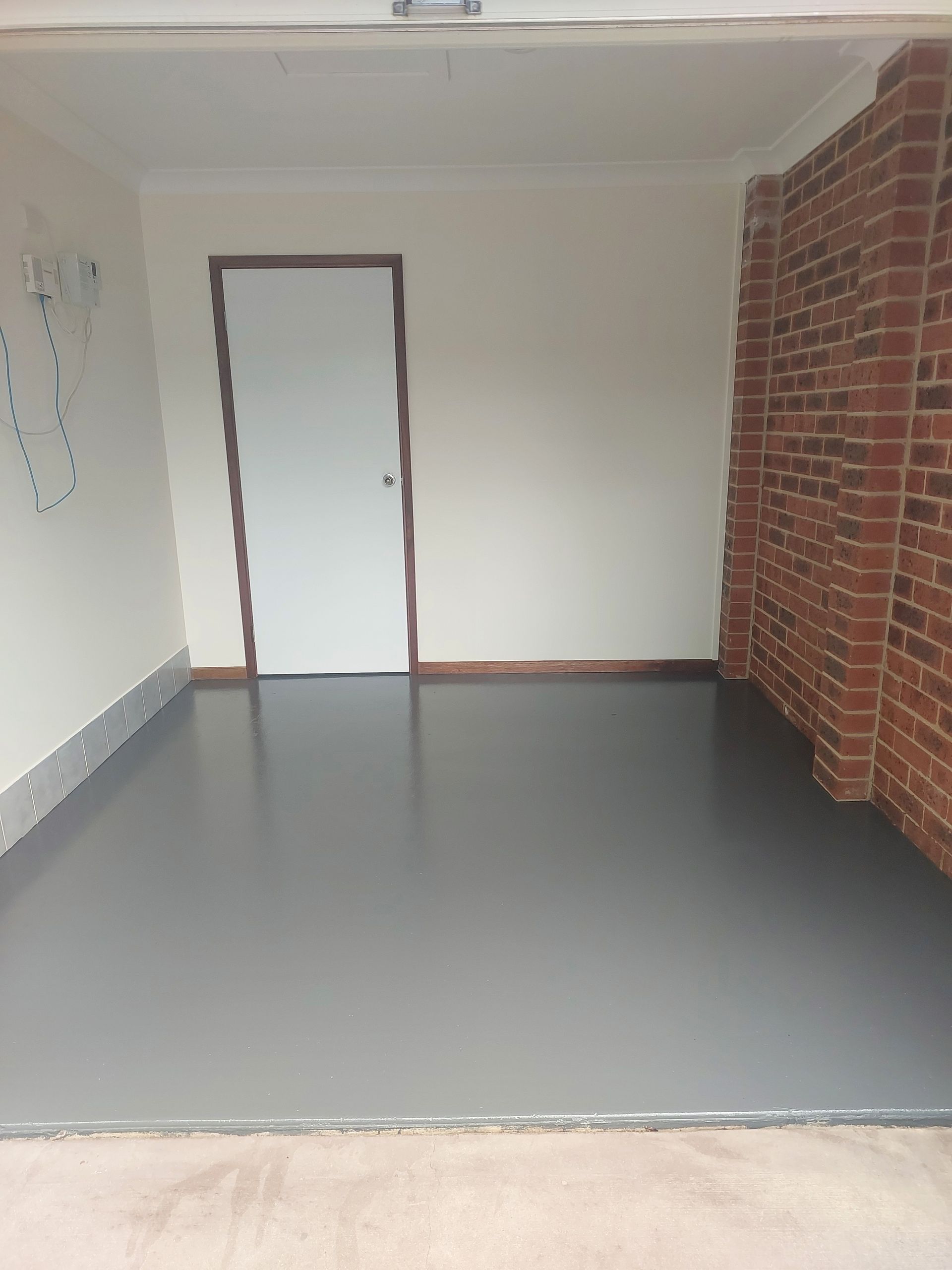 Empty Garage With Gray Floor, White Walls, Brick Column, and White Door — Elimar Construction in Goulburn, NSW