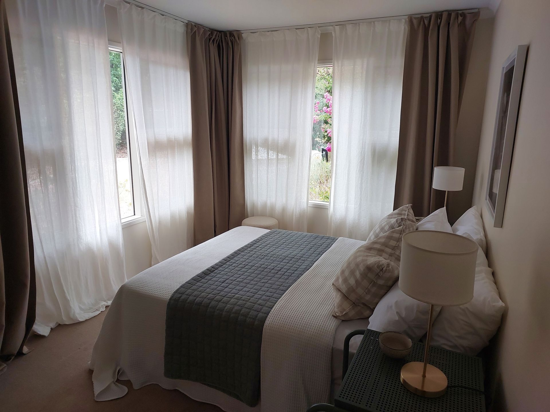 Bedroom With Bed, Windows, and Curtains. White and Brown Curtains Frame Three Windows — Elimar Construction in Goulburn, NSW