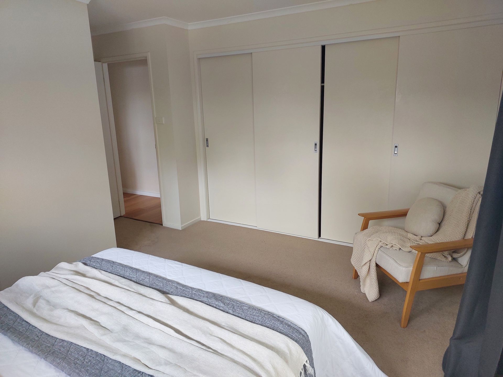 Bedroom With Bed, Closet, Armchair, and Open Doorway. Neutral Colors: White, Beige, Brown — Elimar Construction in Goulburn, NSW