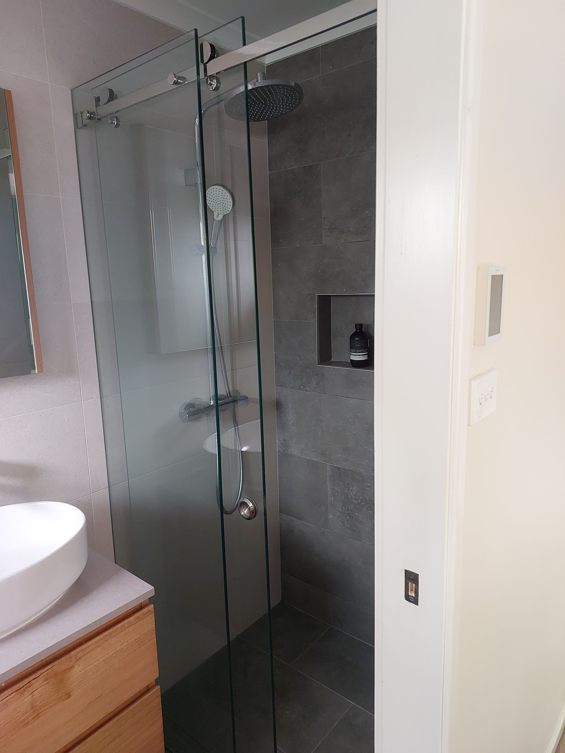Modern Bathroom With Glass Shower Enclosure, Gray Tile, and Wooden Vanity — Elimar Construction in Goulburn, NSW