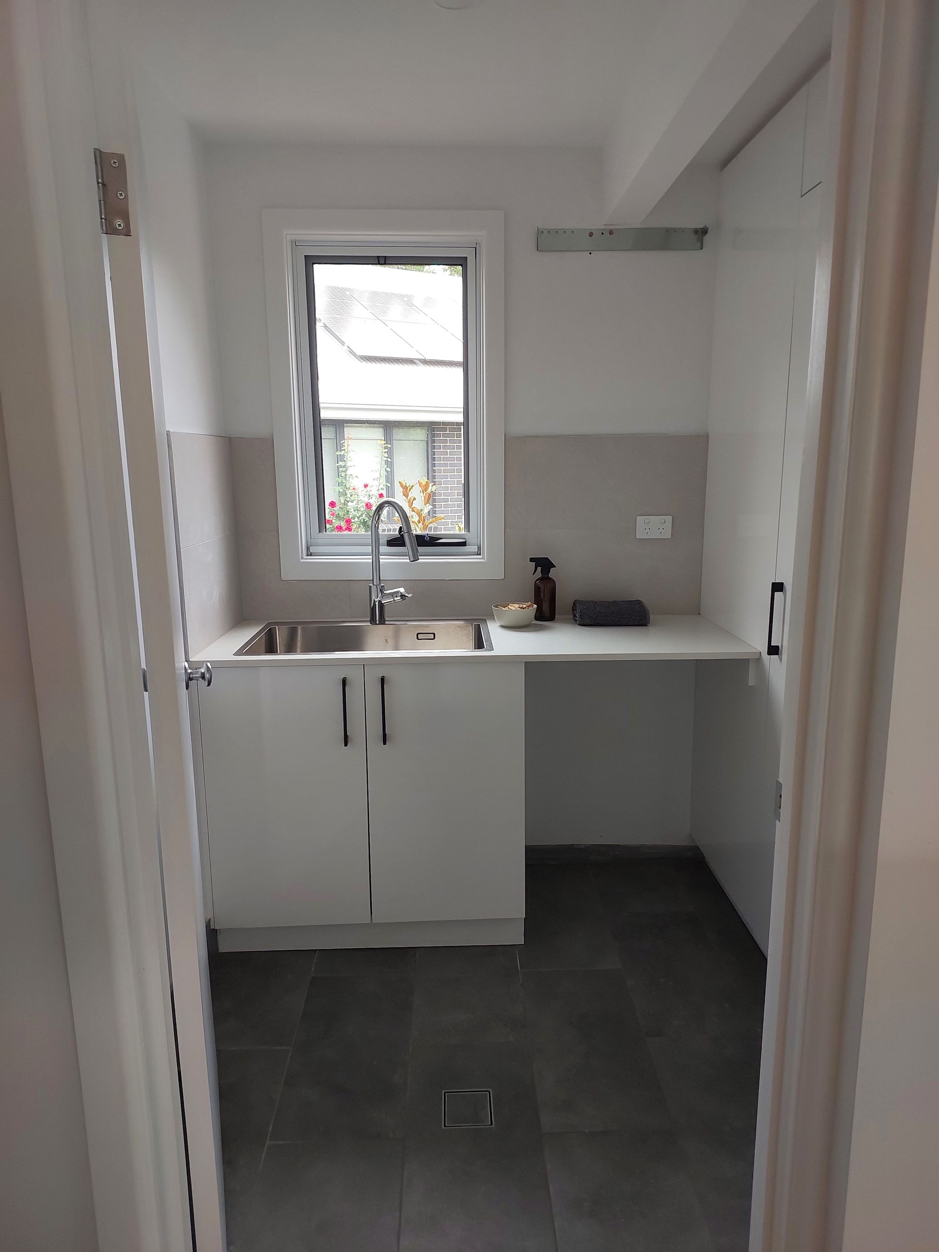 Small Laundry Room With White Cabinets, Stainless Steel Sink, and Gray Floor Tiles — Elimar Construction in Goulburn, NSW