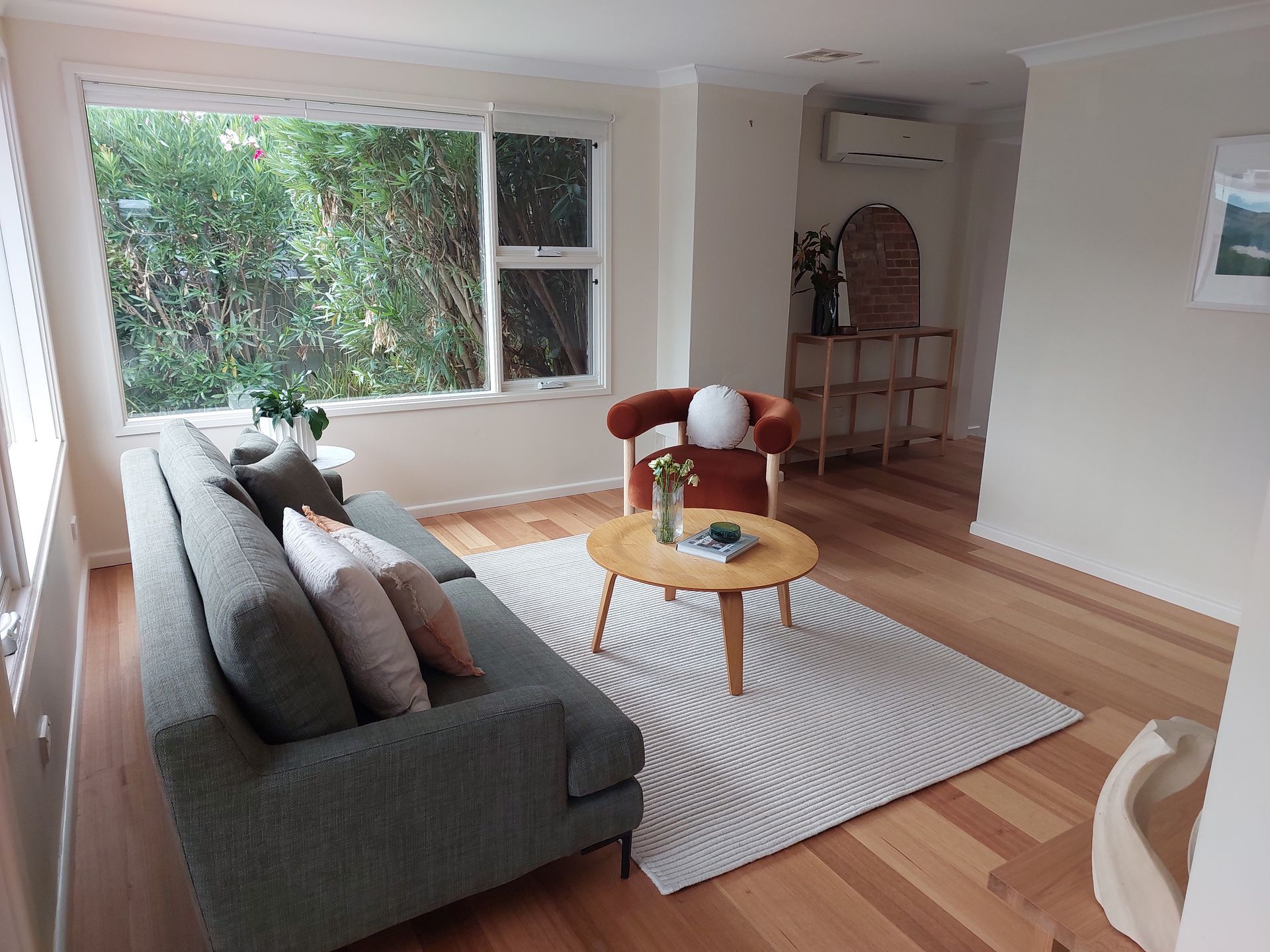 Living Room With Gray Sofa, Orange Chair, Wooden Floor, Large Window, and Rug — Elimar Construction in Goulburn, NSW