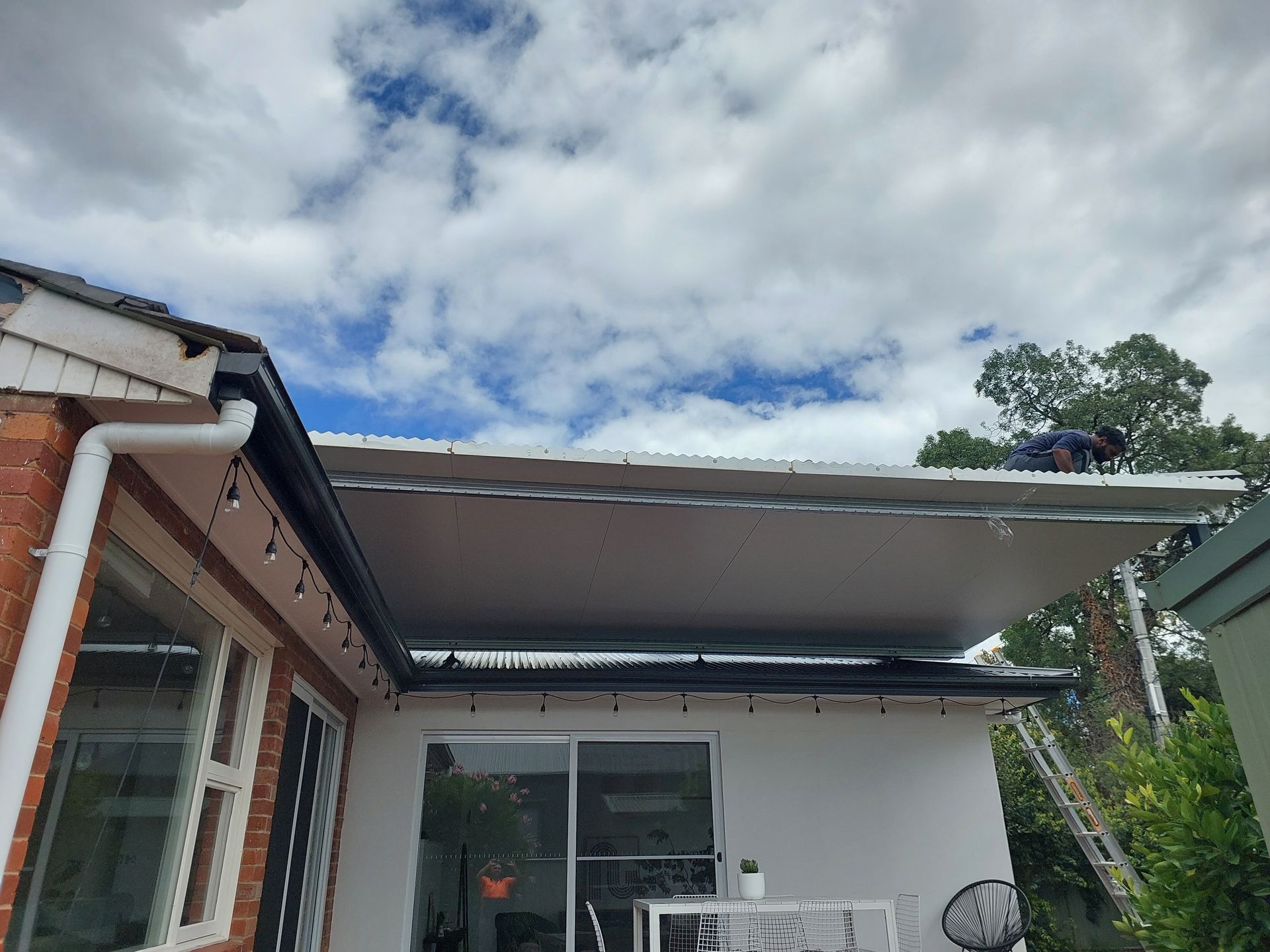 Man Working on a White Awning Attached to a House With a Cloudy Sky Overhead — Elimar Construction in Goulburn, NSW