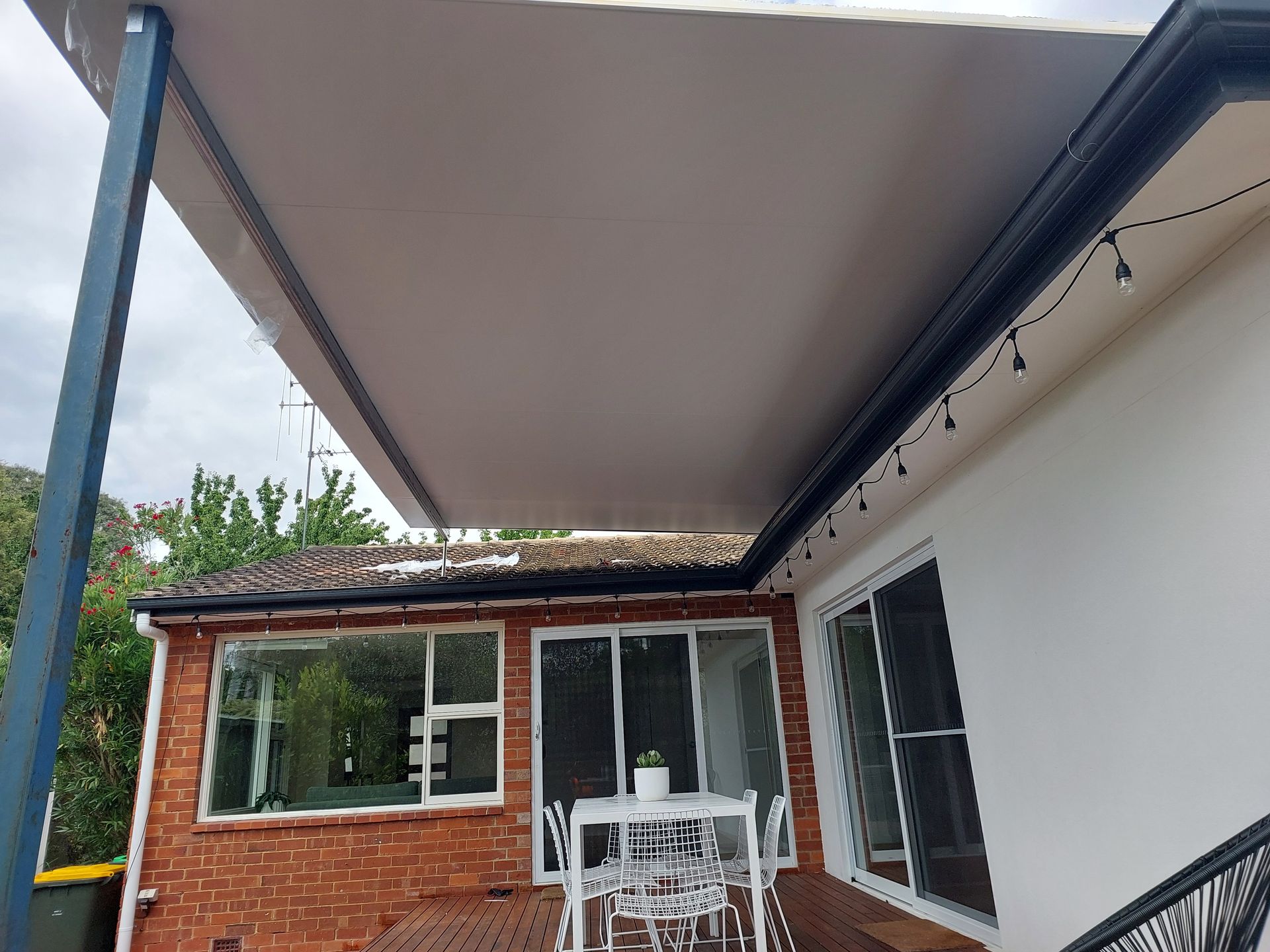 Outdoor Patio With a Retractable Awning, Brick Building, and White Table Set — Elimar Construction in Goulburn, NSW