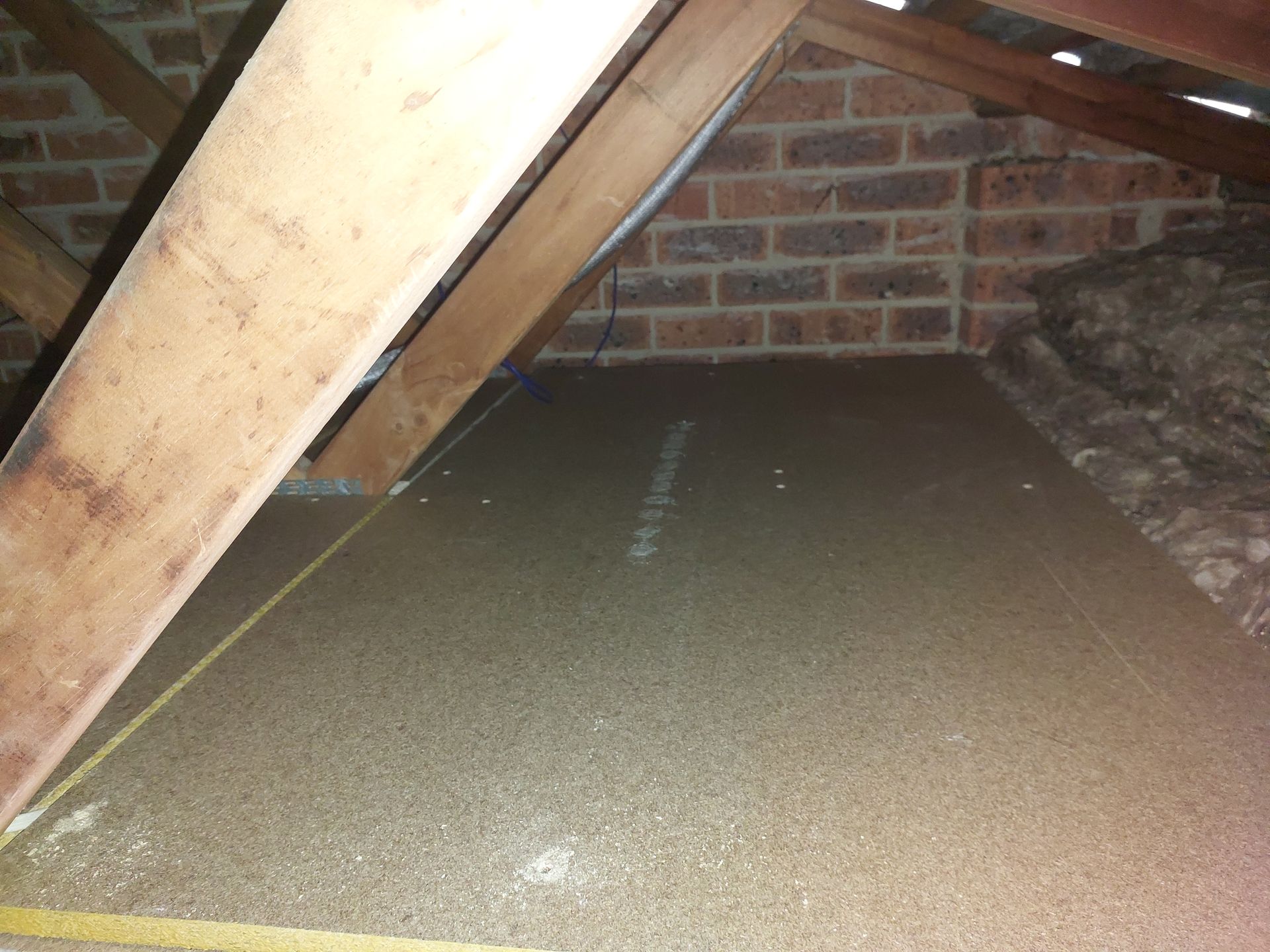 Attic Space With Wooden Beams, Brick Wall, and Insulation Layer on the Floor — Elimar Construction in Goulburn, NSW