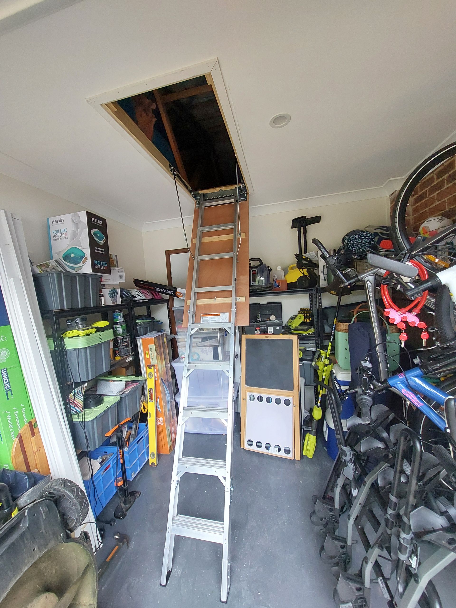 a Cluttered Garage With a Ladder Leading to an Attic Access. Various Stored Items Surround the Ladder — Elimar Construction in Goulburn, NSW