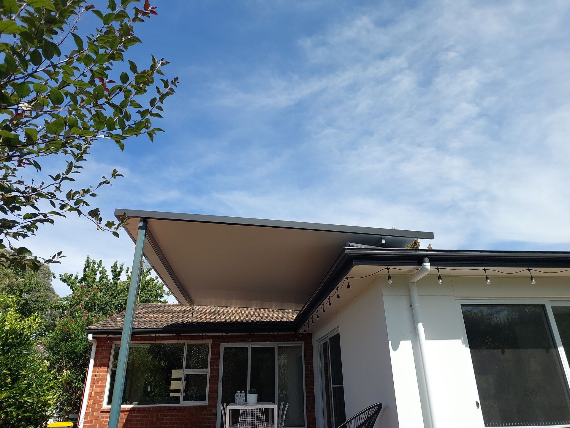 Beige Patio Cover Attached to a White House With a Blue Sky Background — Elimar Construction in Goulburn, NSW