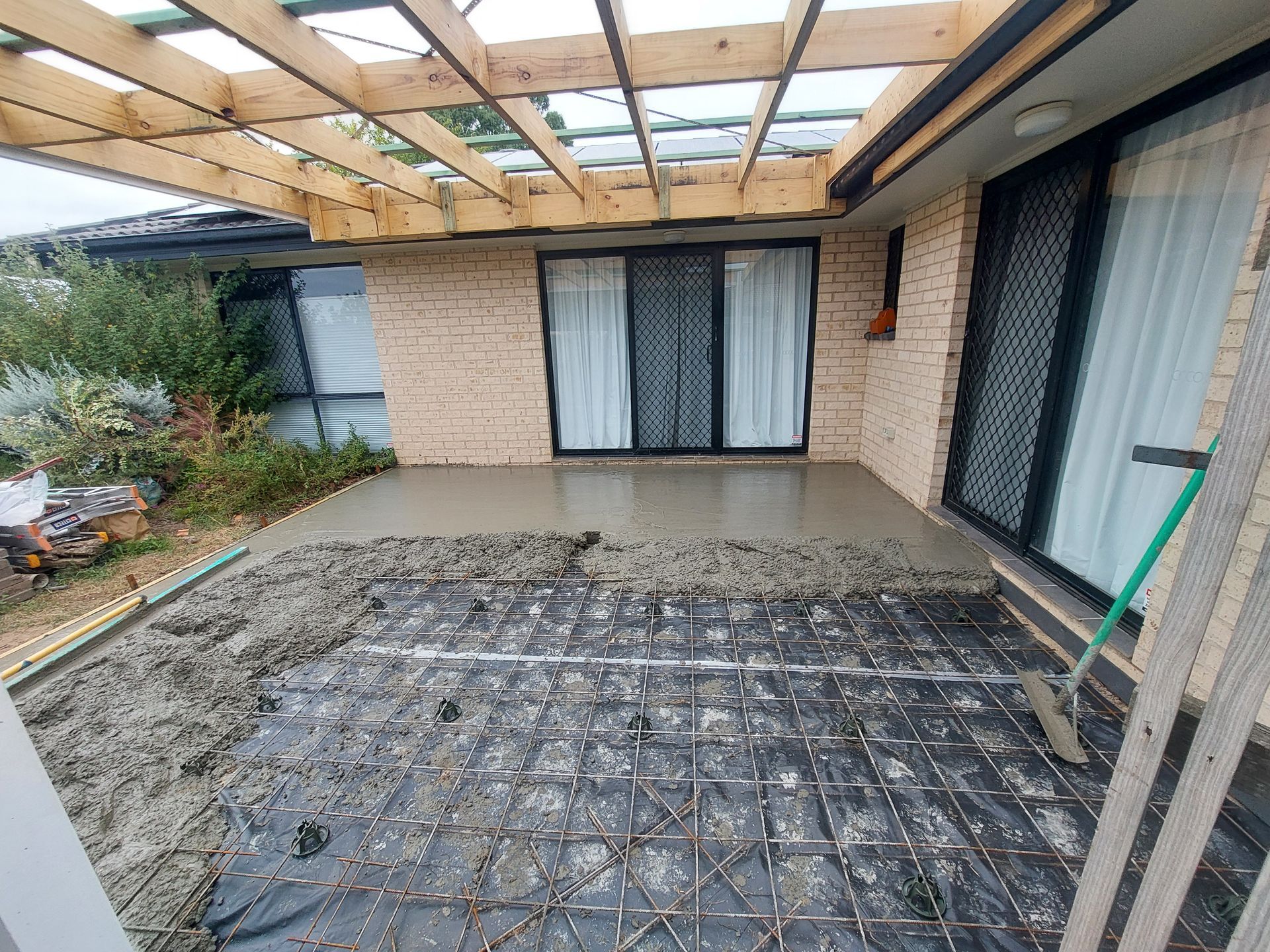 Concrete Patio Under Construction; Rebar Grid Laid, Partially Covered by Wet Concrete, Beside a Brick House — Elimar Construction in Goulburn, NSW