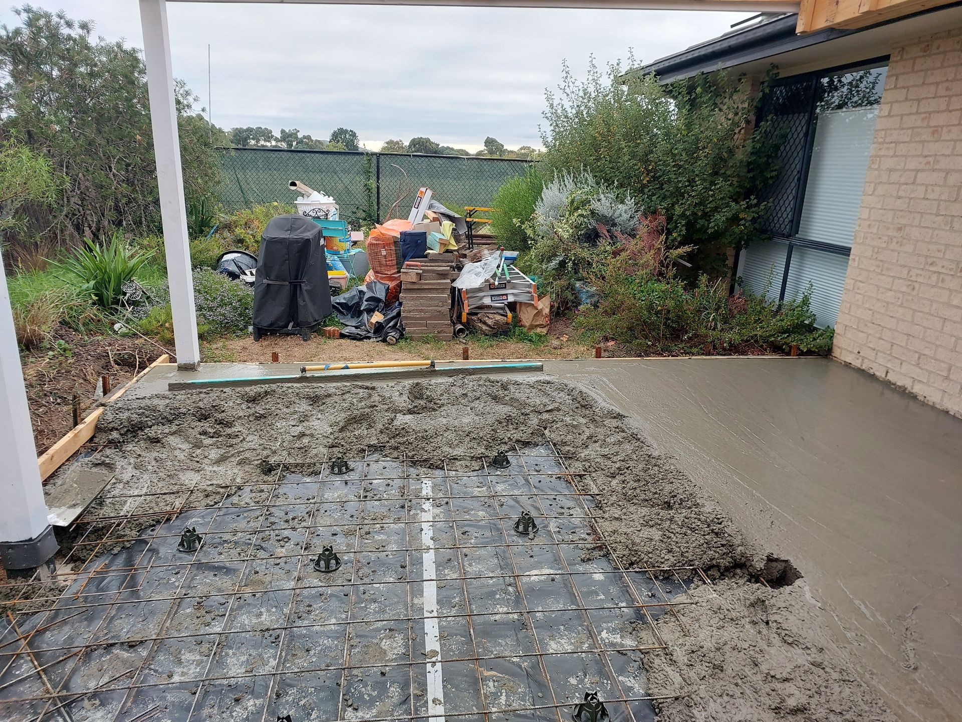 Fresh Concrete Patio Being Poured With Construction Debris in the Background — Elimar Construction in Goulburn, NSW
