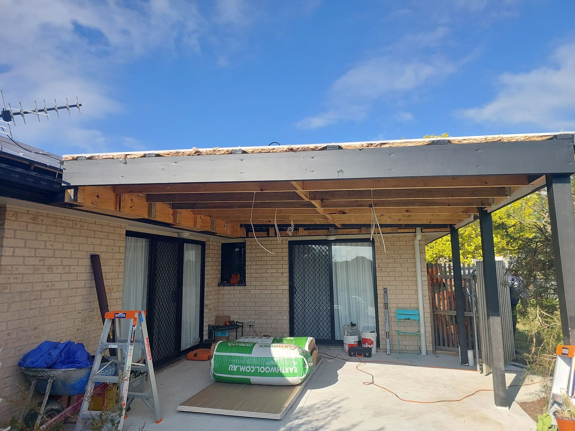 Patio Roof Under Construction; Exposed Wooden Beams, Brick Wall, and Blue Sky — Elimar Construction in Goulburn, NSW