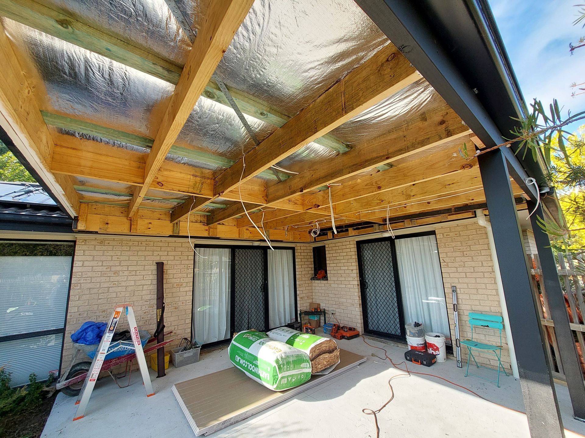 Patio Roof Under Construction With Wooden Beams, Insulation, and Brick Wall — Elimar Construction in Goulburn, NSW