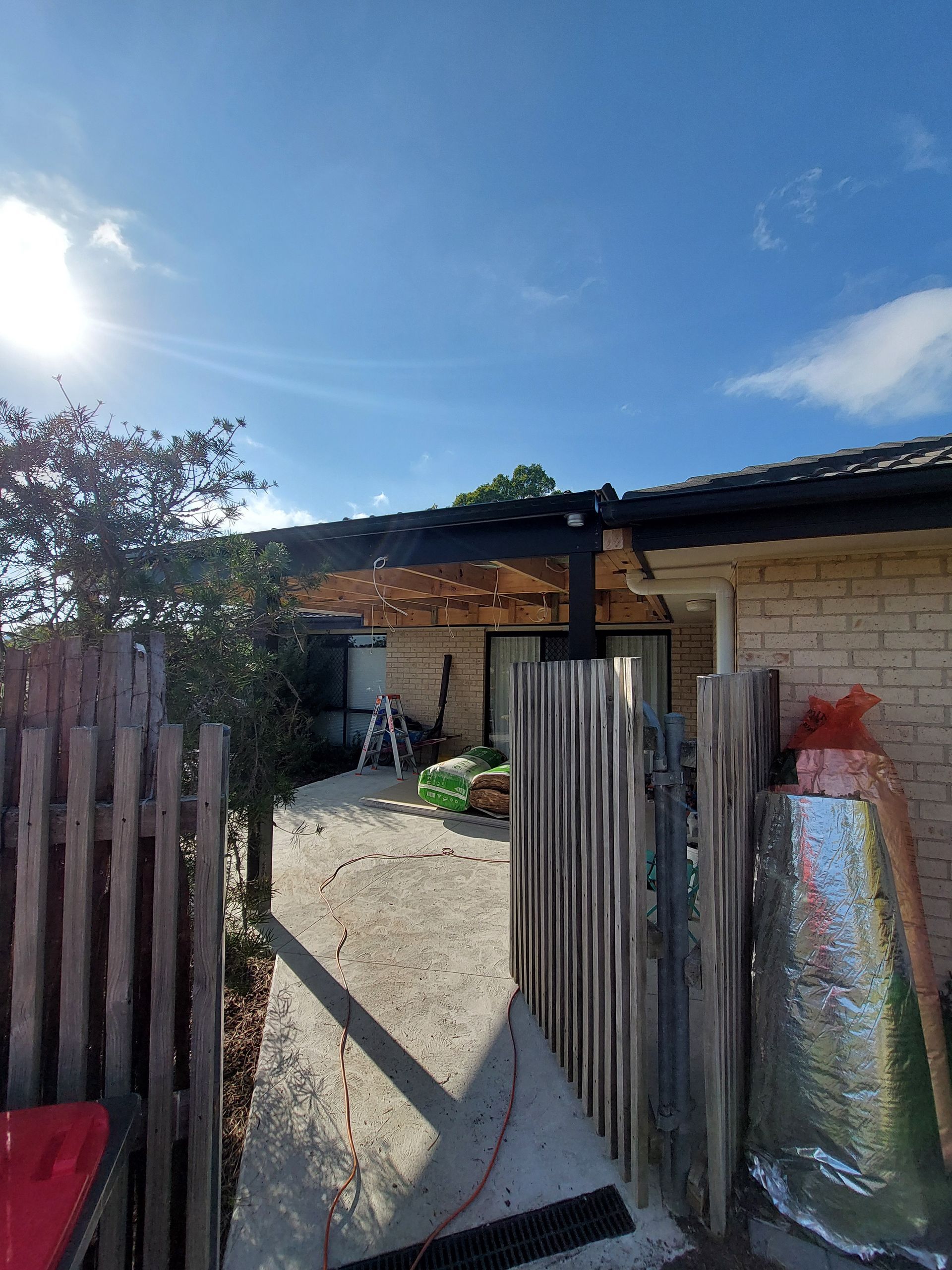 Entryway With Damaged Pergola, Exposed Roof Structure, Brick Building, and Wooden Fence on a Sunny Day — Elimar Construction in Goulburn, NSW