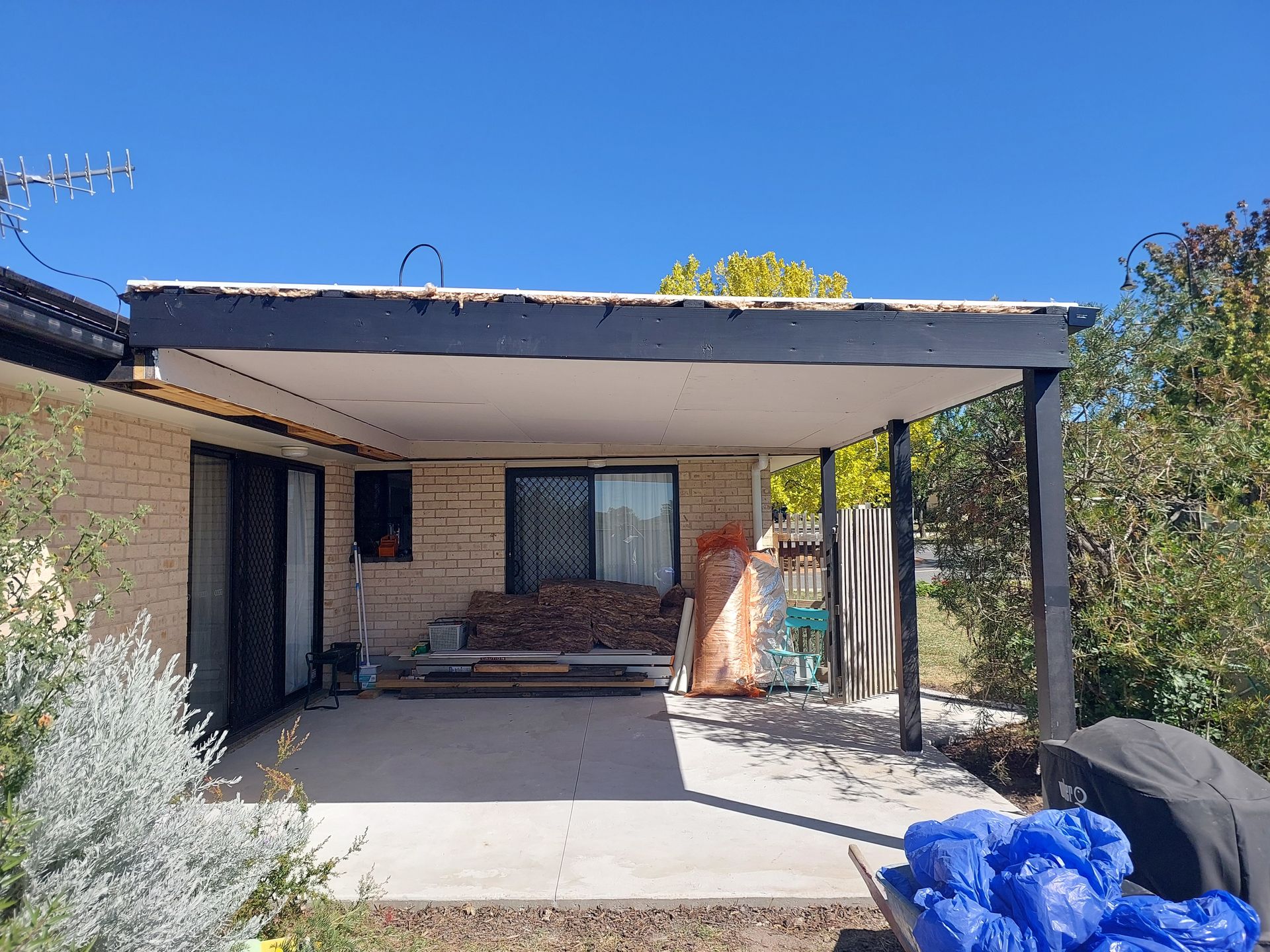 Backyard Patio With a Concrete Floor, Attached to a Brick Home Under a Dark-trimmed Roof, With Debris — Elimar Construction in Goulburn, NSW