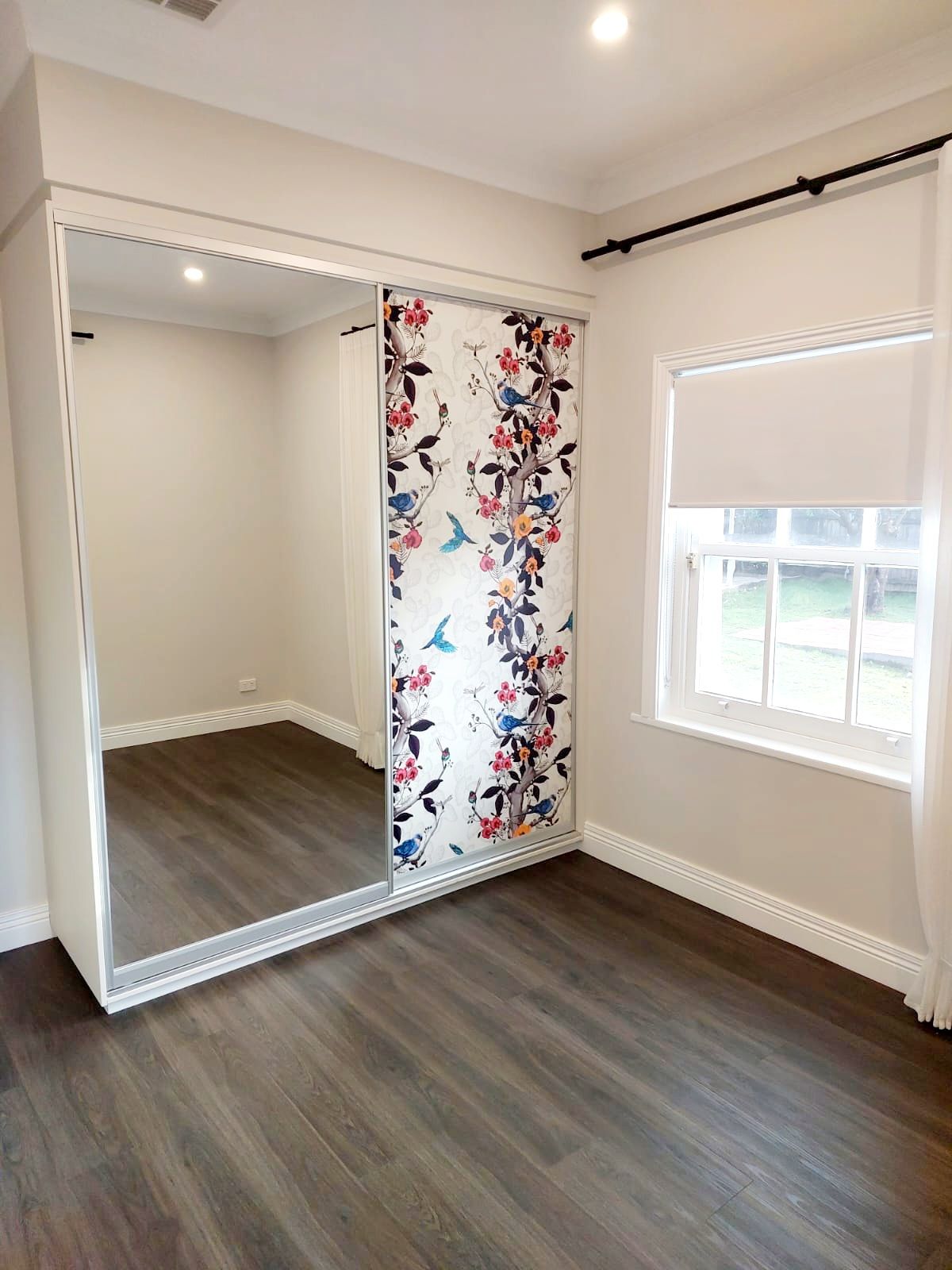 Bedroom With Dark Wood-look Floor, White Walls, and a Sliding Door Wardrobe With Mirror and Floral Design  — Elimar Construction in Goulburn, NSW