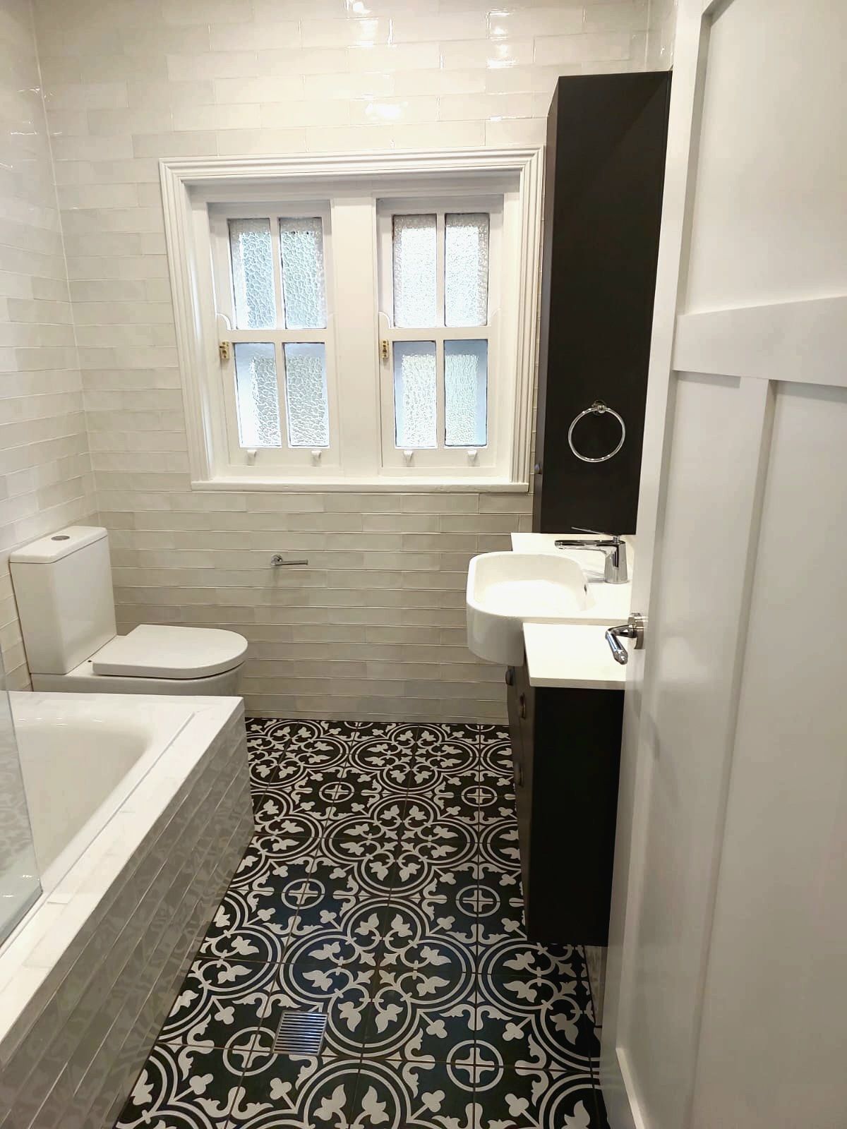 Bathroom With Black and White Patterned Floor, White Walls, Toilet, Sink, and Tall Black Cabinet  — Elimar Construction in Goulburn, NSW