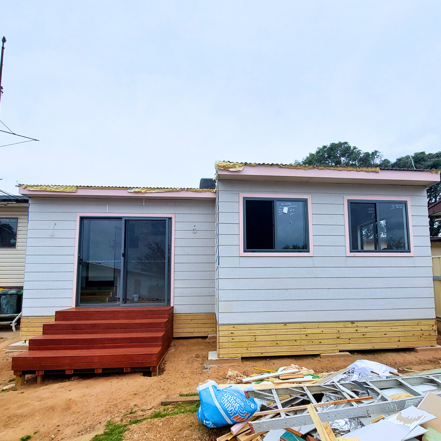 A Small, Light Gray Building With a Red Wooden Deck and Sliding Glass Door — Elimar Construction in Goulburn, NSW