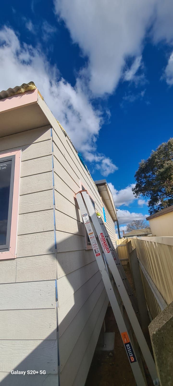 Ladder Leaning Against a House With Light-colored Siding, Under a Bright Blue Sky With Clouds — Elimar Construction in Goulburn, NSW