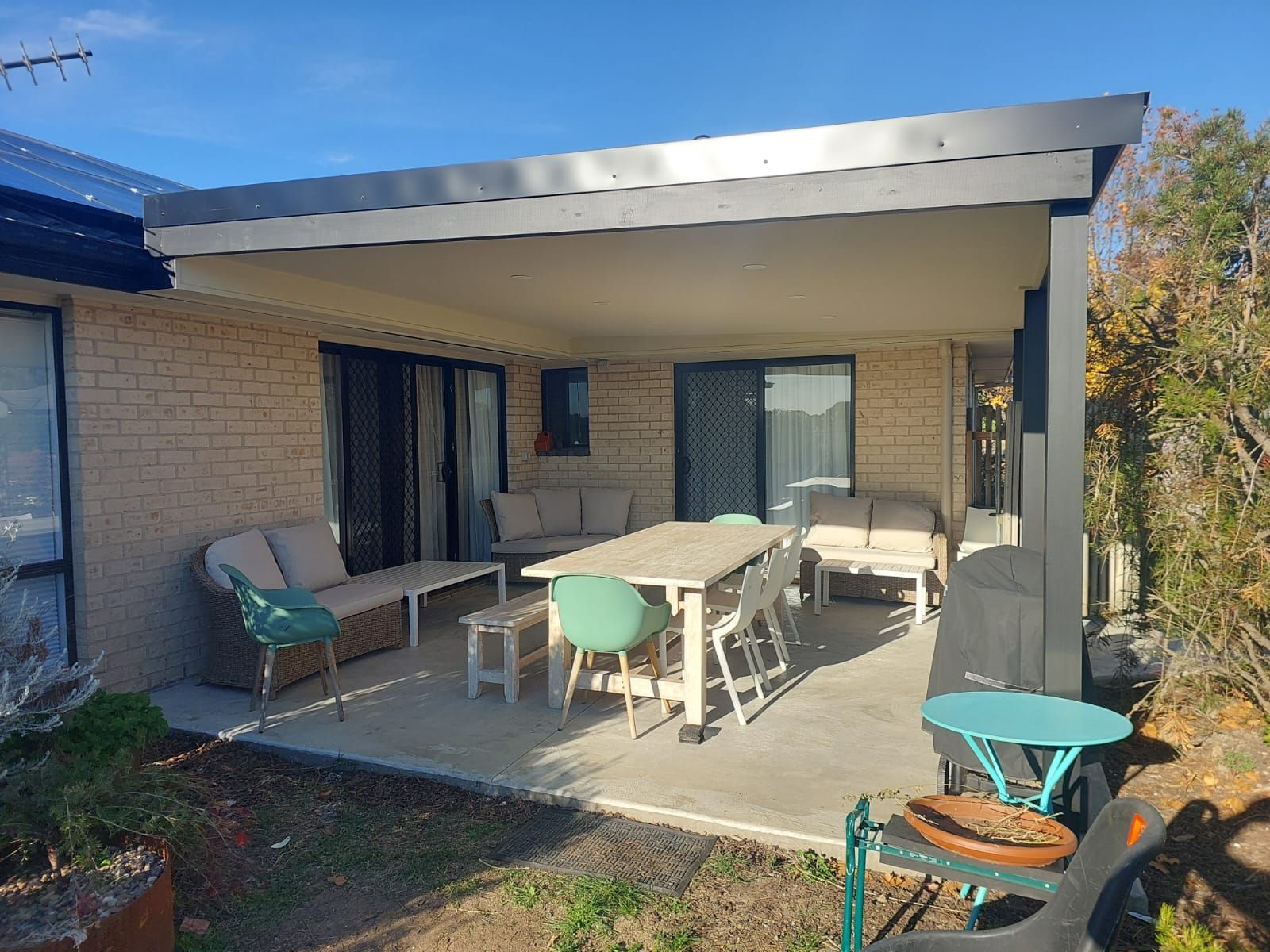 Patio With Outdoor Furniture Under a Gray Awning. Beige Brick House, Sunny Day — Elimar Construction in Goulburn, NSW